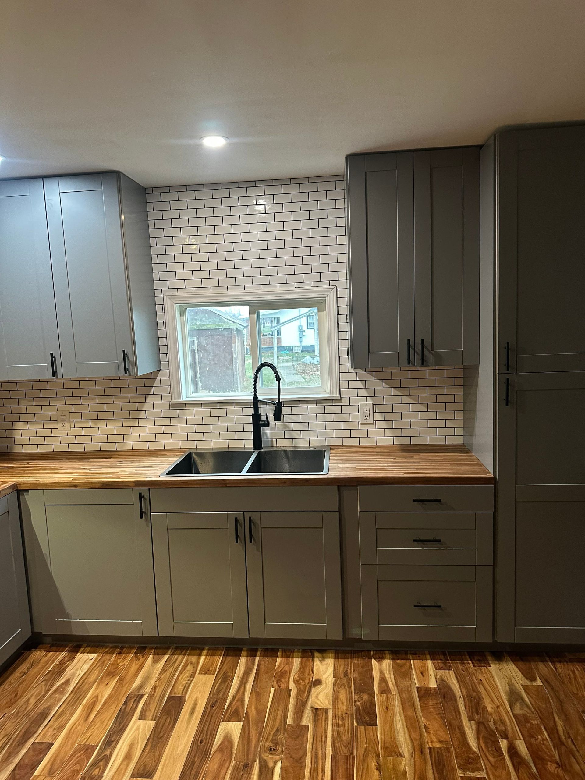 Modern kitchen with gray cabinets, wood countertops, tiled backsplash, sink, and hardwood floor