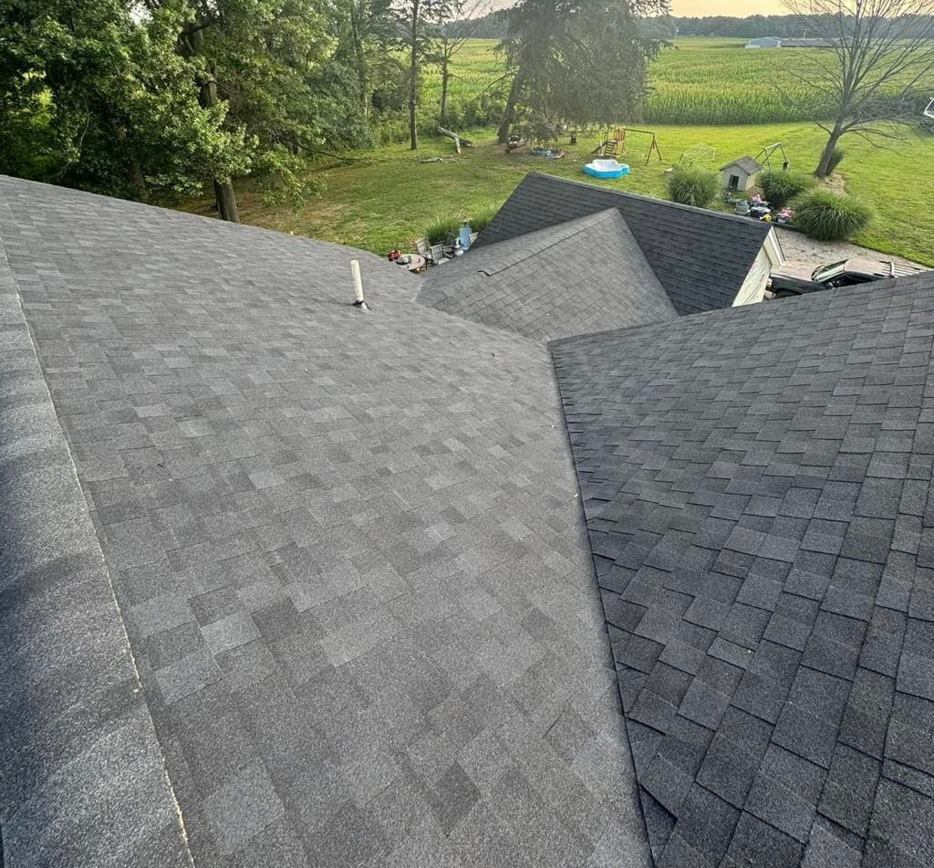 Gray shingled rooftops overlooking a green countryside garden and fields