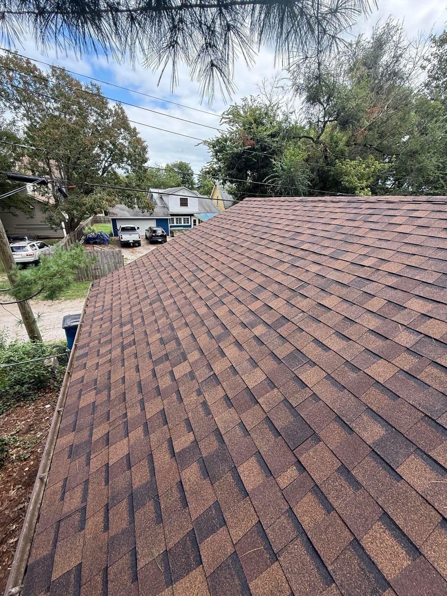 Shingled roof in foreground with trees, a driveway, and houses in the background