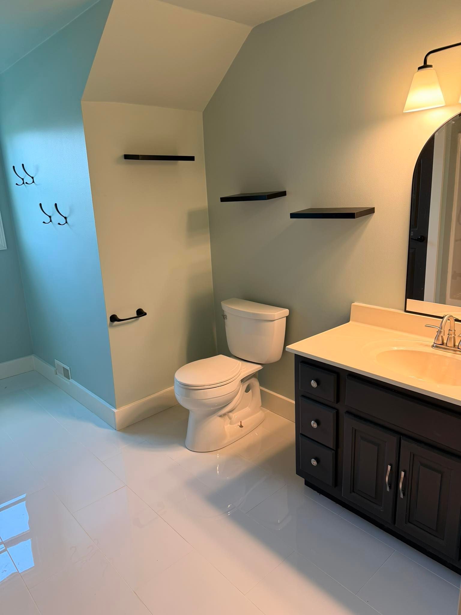 Bathroom with toilet, sink vanity, wall shelves, and tiled shower in a modern light-blue room