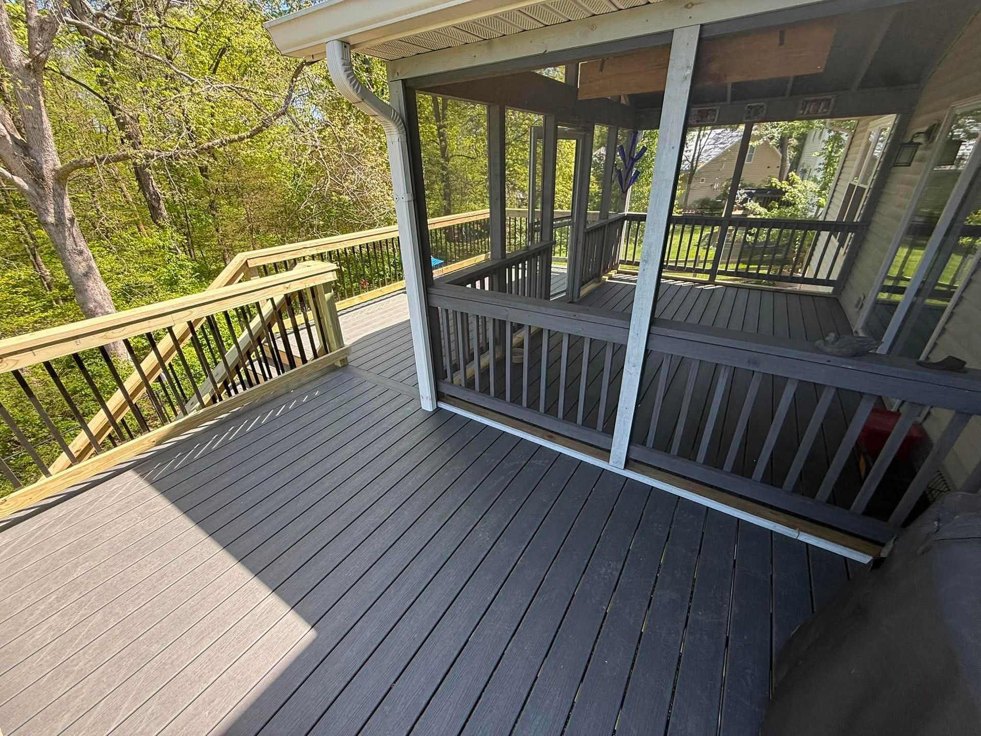 Wooden deck with black railing and screened porch, overlooking trees on a sunny day