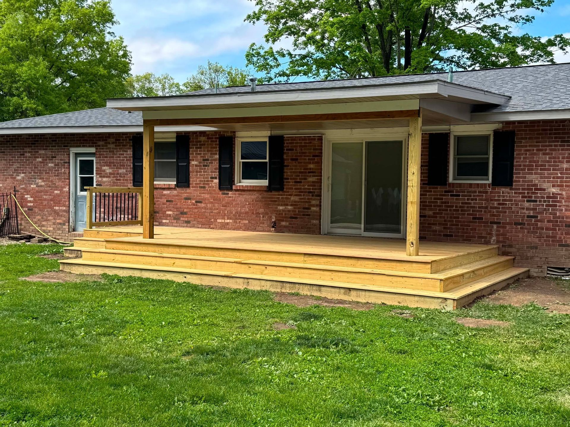 Brick house porch with fresh wooden steps and a covered entry above a green lawn