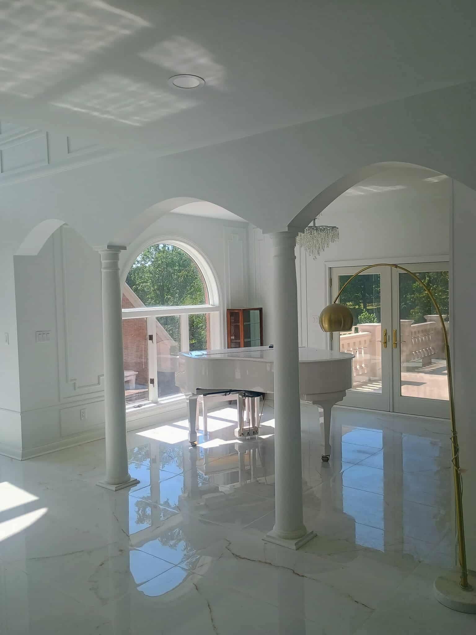 Bright white living room with arched openings, reflective tile floor, and patio doors leading to a sunny backyard.