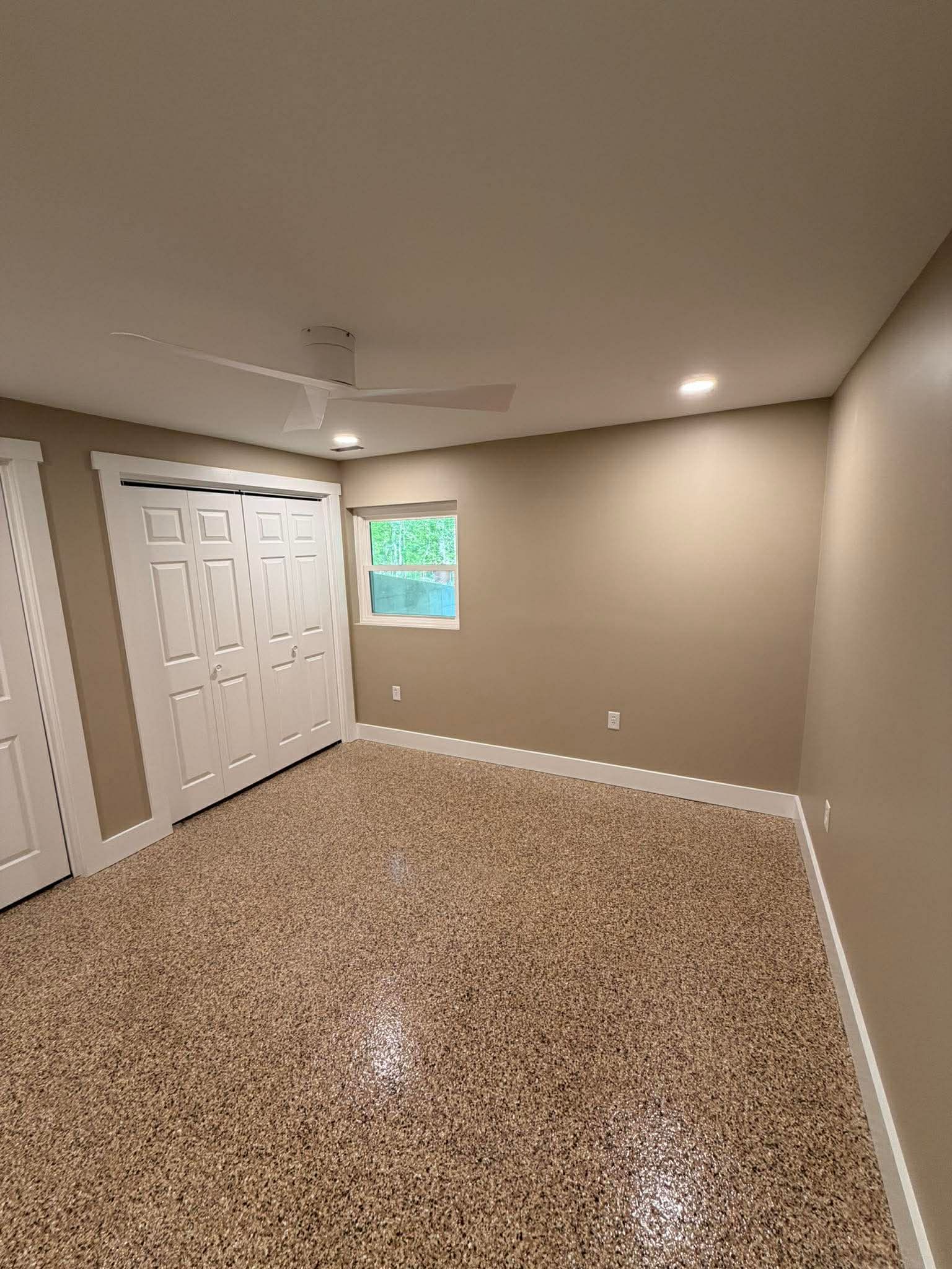 Empty carpeted room with beige walls, white closet doors, and a small window.