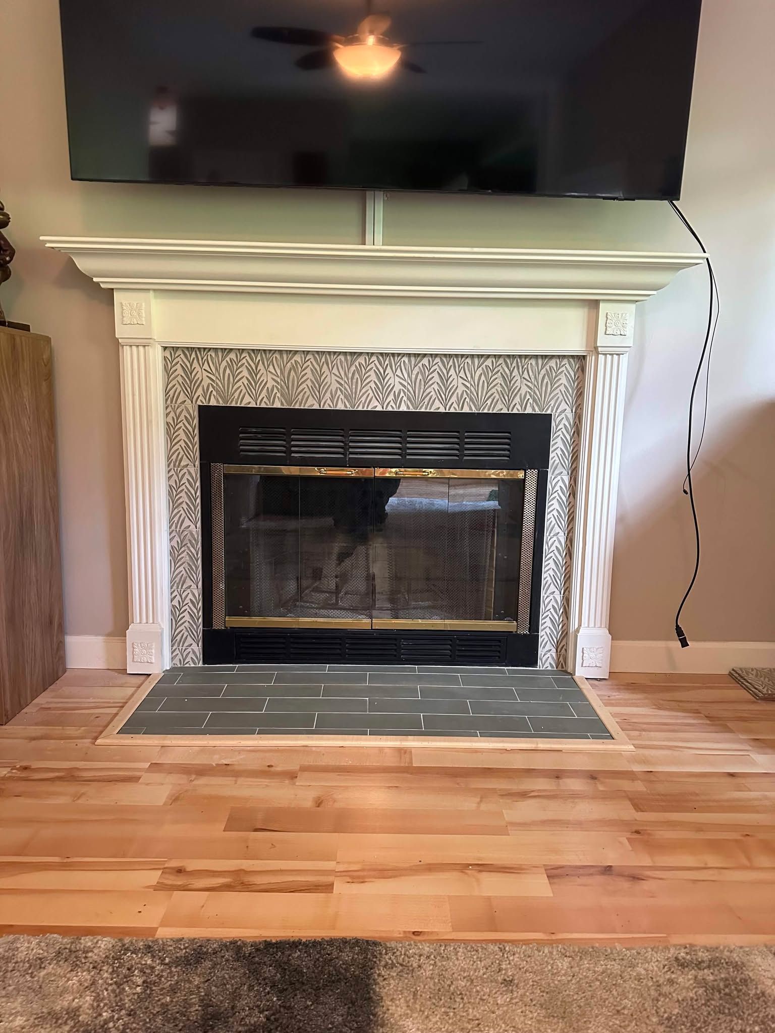 Living room fireplace with white mantel, black screen, hardwood floor, and wall-mounted TV above