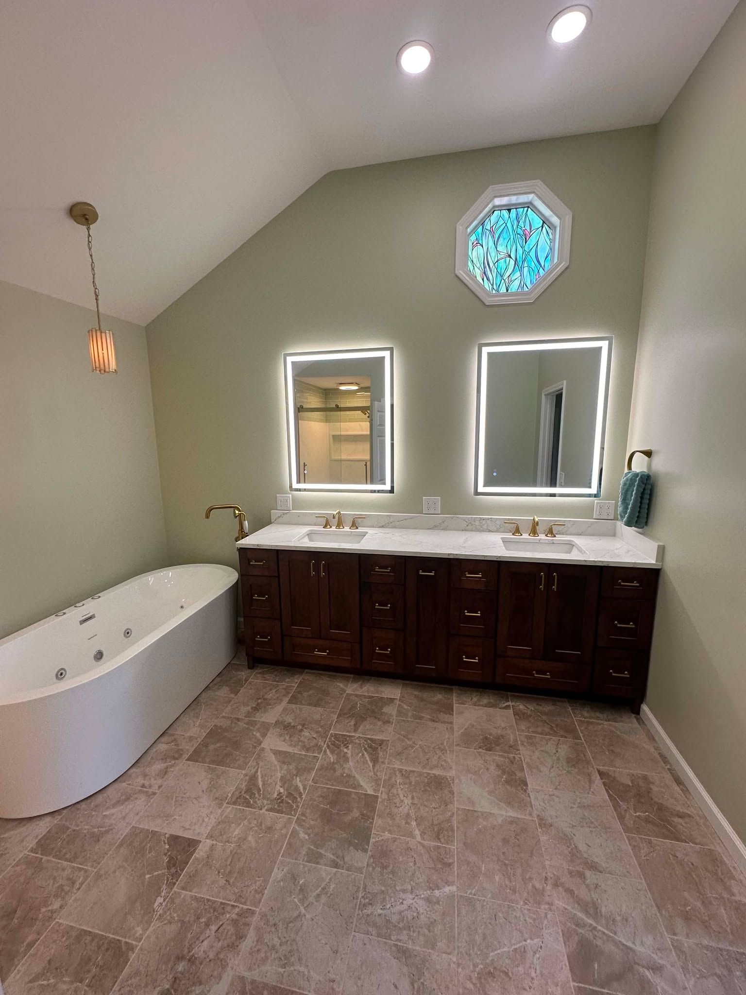 Modern bathroom with double vanity, white tub, beige tile floor, and small octagonal window above the sinks