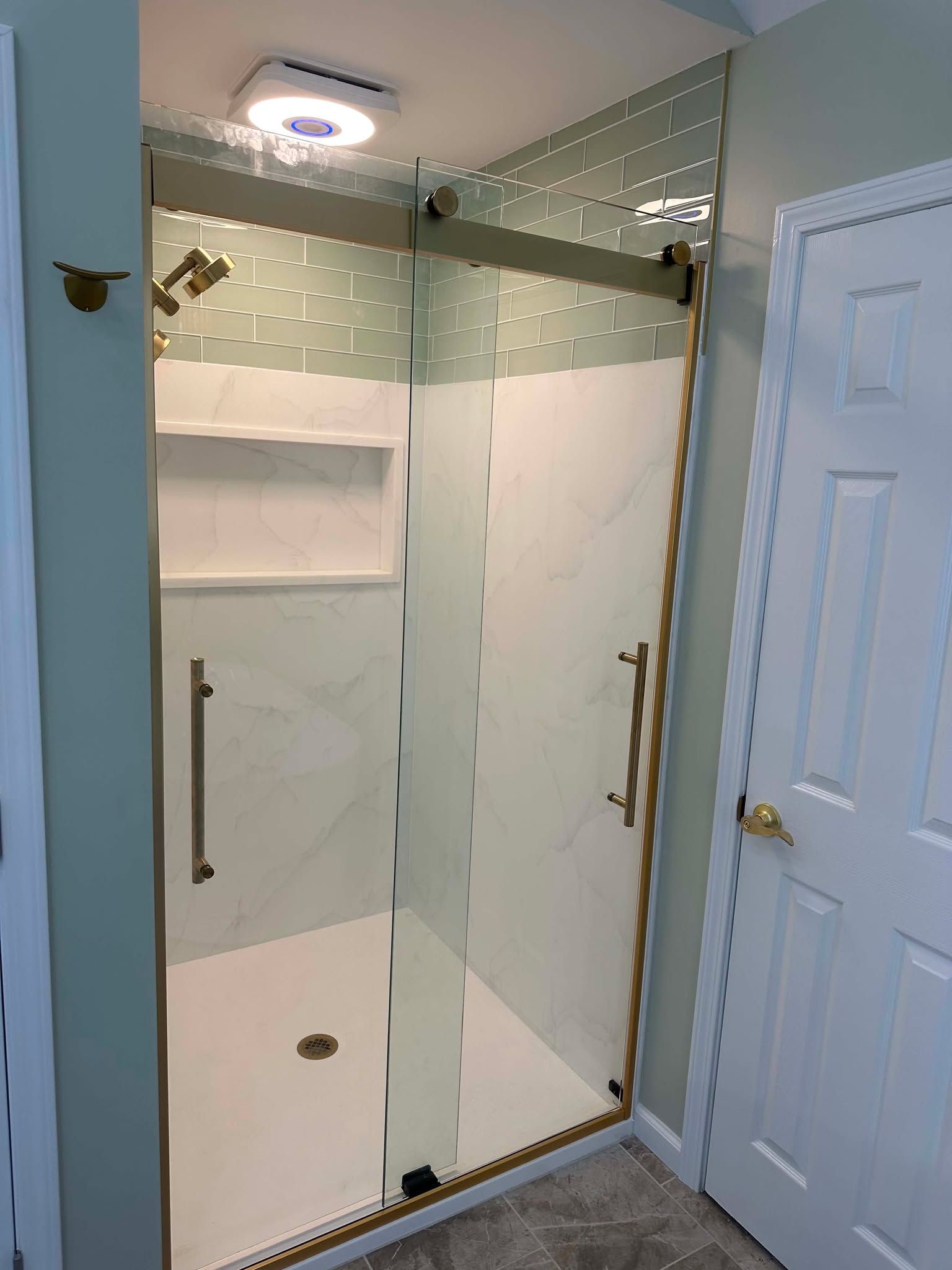 Compact bathroom shower with glass doors, white walls, and a ceiling light near a white door