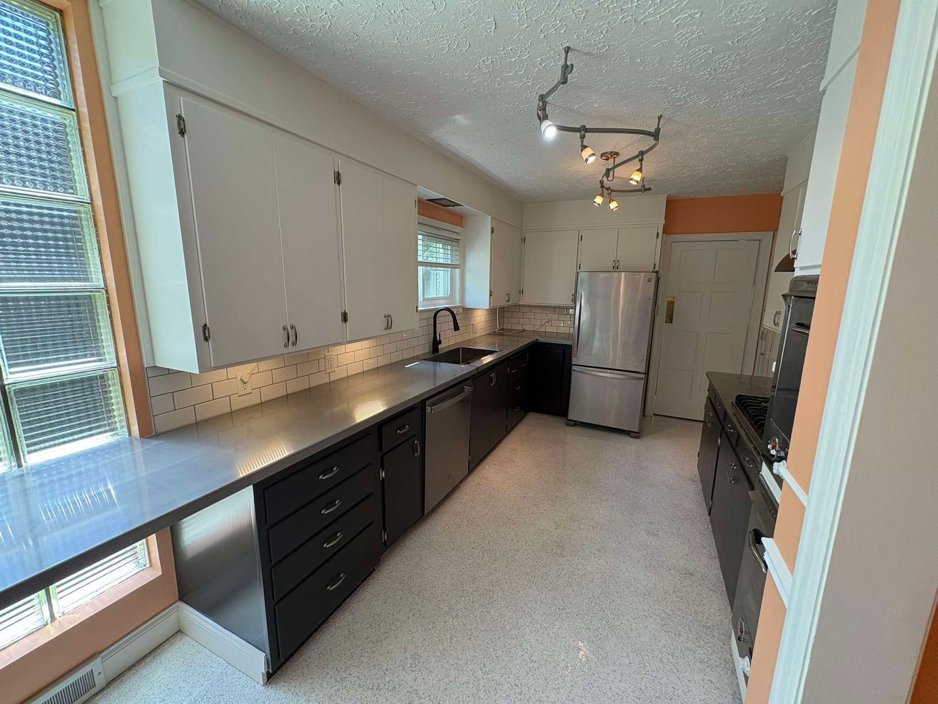Modern galley kitchen with dark counters, white cabinets, and a stainless refrigerator under track lighting