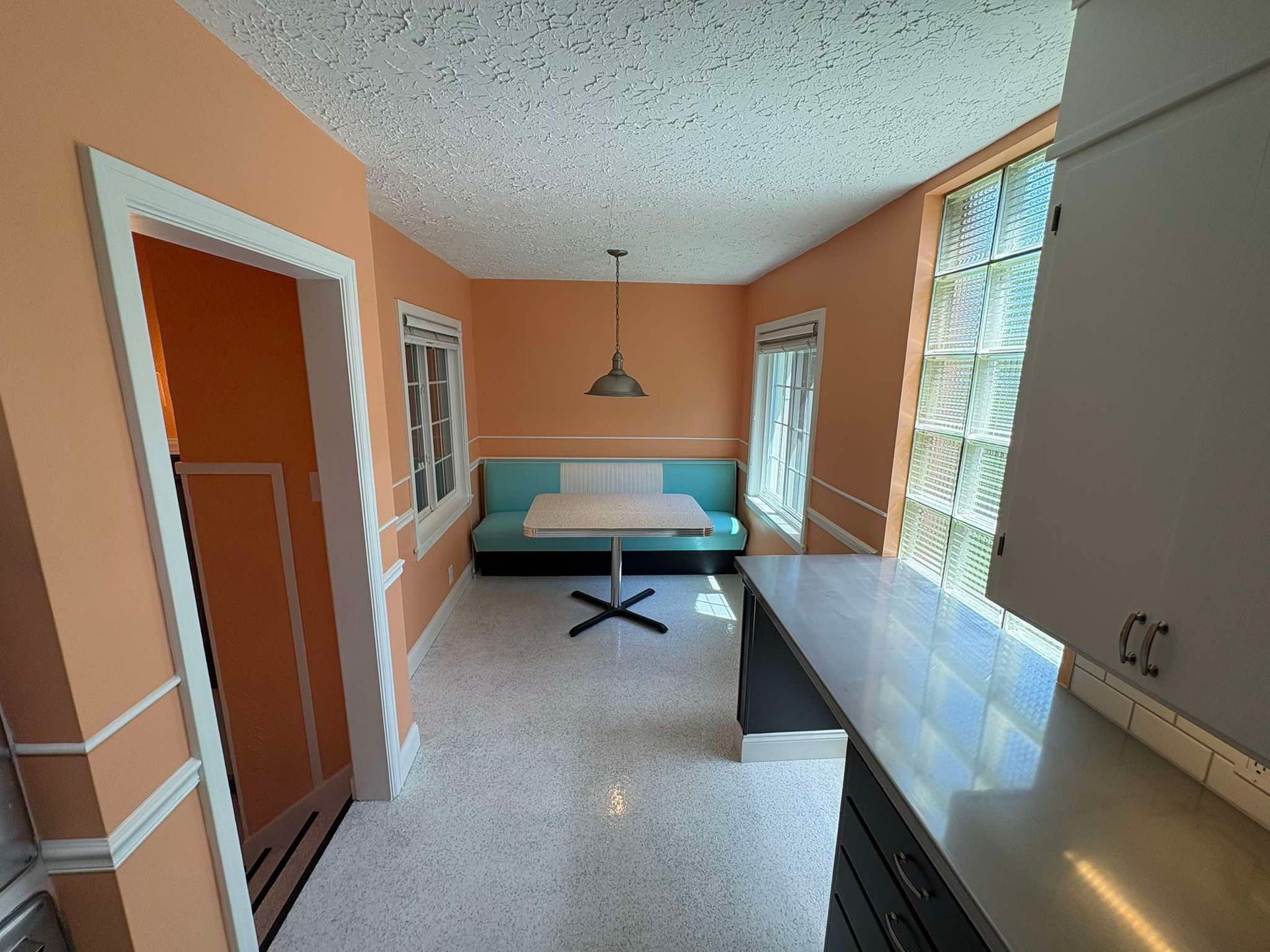 Bright sunroom with teal daybed, orange walls, long windows, and a countertop along the right side.
