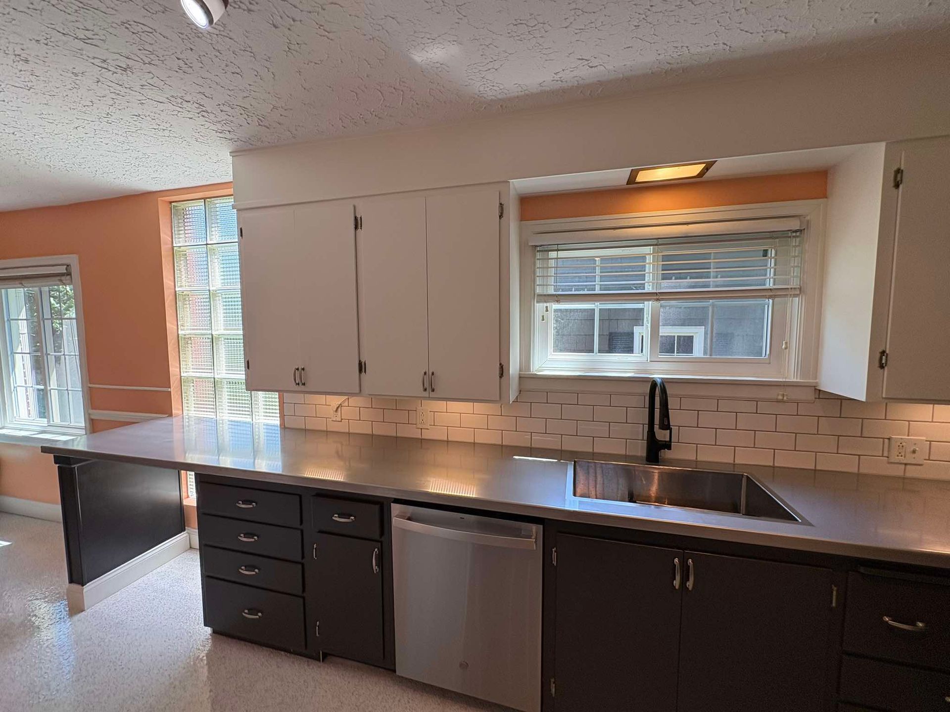 Modern kitchen with white cabinets, dark lower cabinets, stainless dishwasher, and a window over the sink