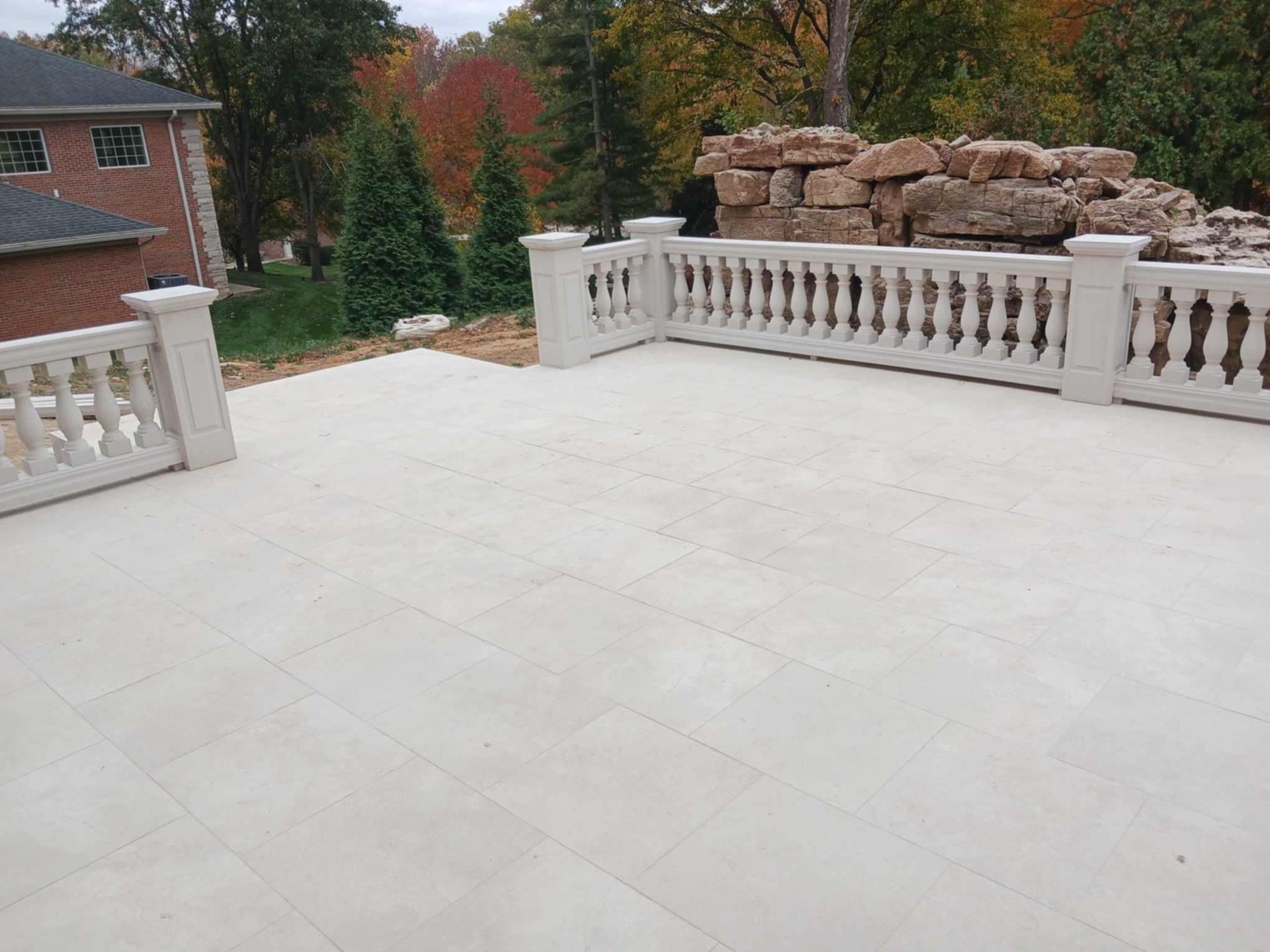 Spacious light stone patio with white balustrade railings and a rock garden beyond