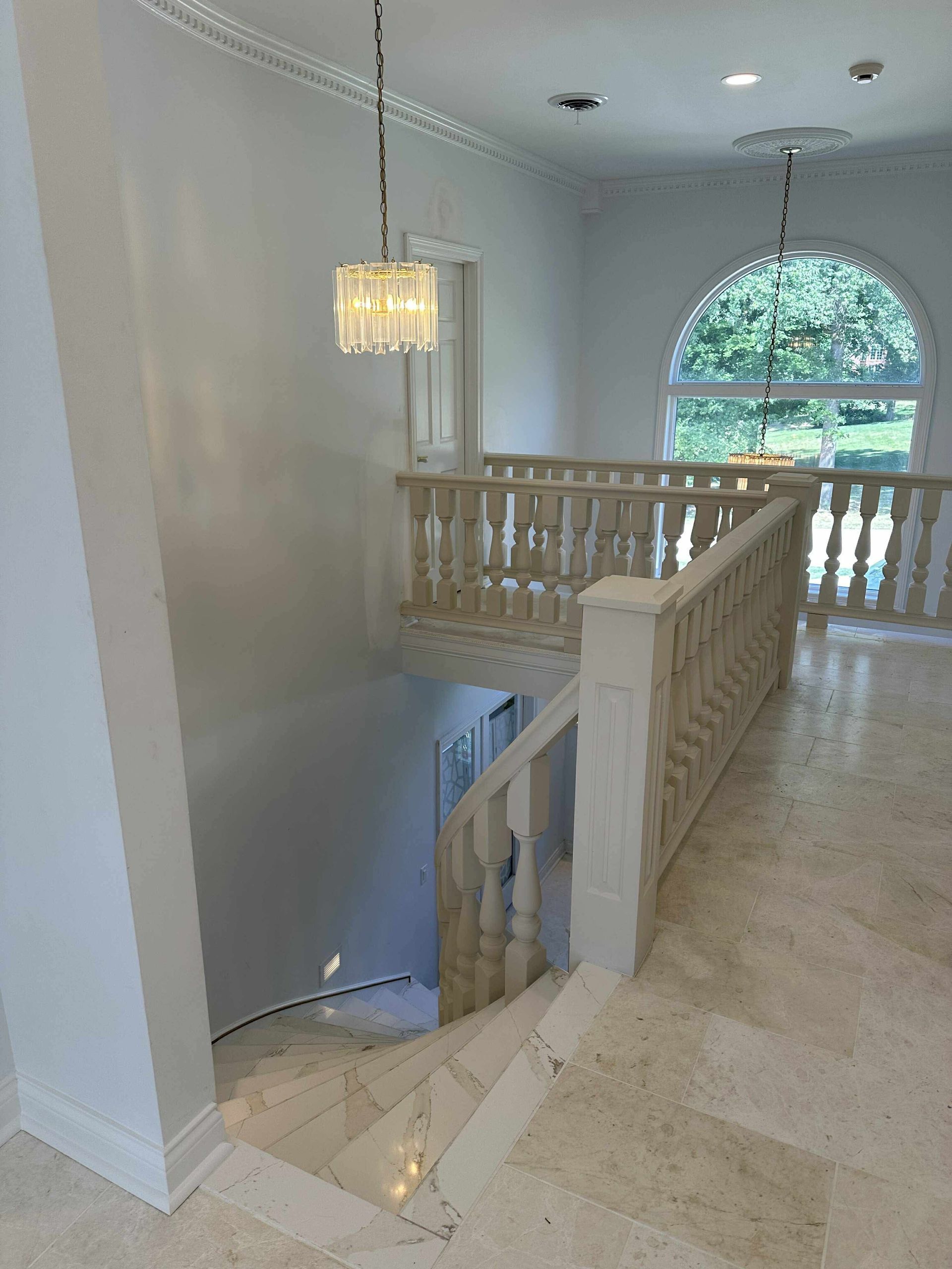 Interior stair landing with white railing, hanging light, and large arched window overlooking trees