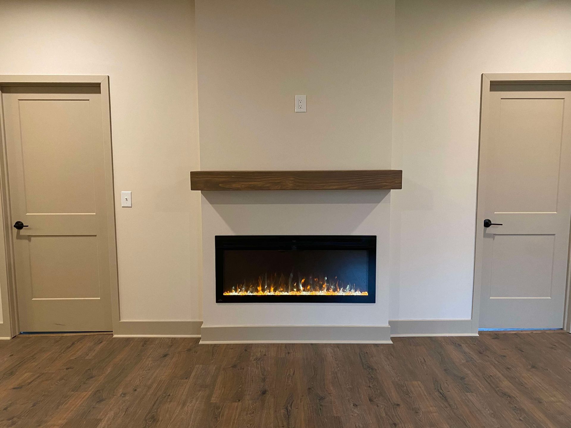 Modern living room with two beige doors and a centered electric fireplace with wooden mantel on a gray wall.
