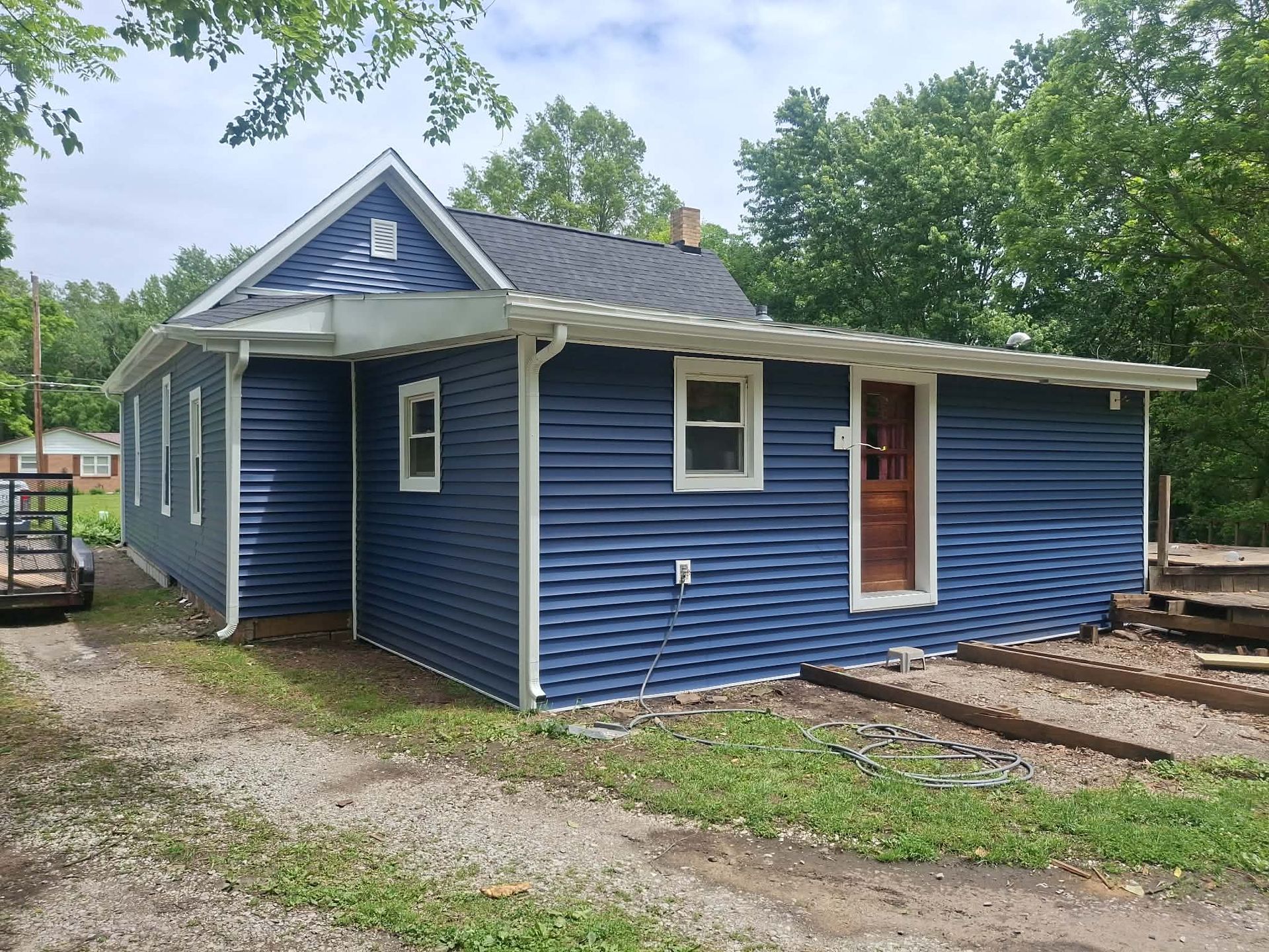 Blue single-story house with white trim and a small porch in a wooded yard