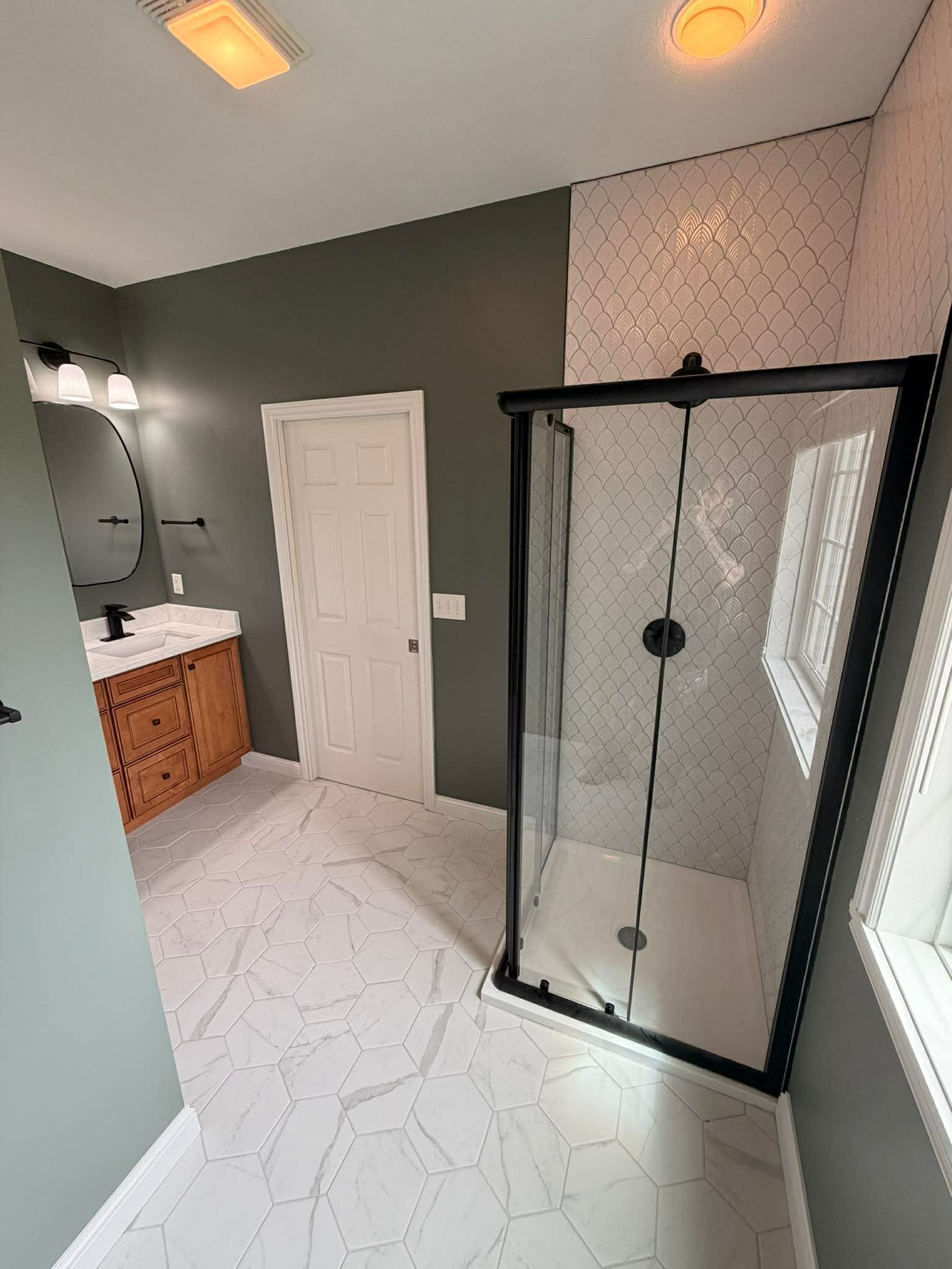 Modern bathroom with glass shower, white marble floor, vanity, and dark green walls