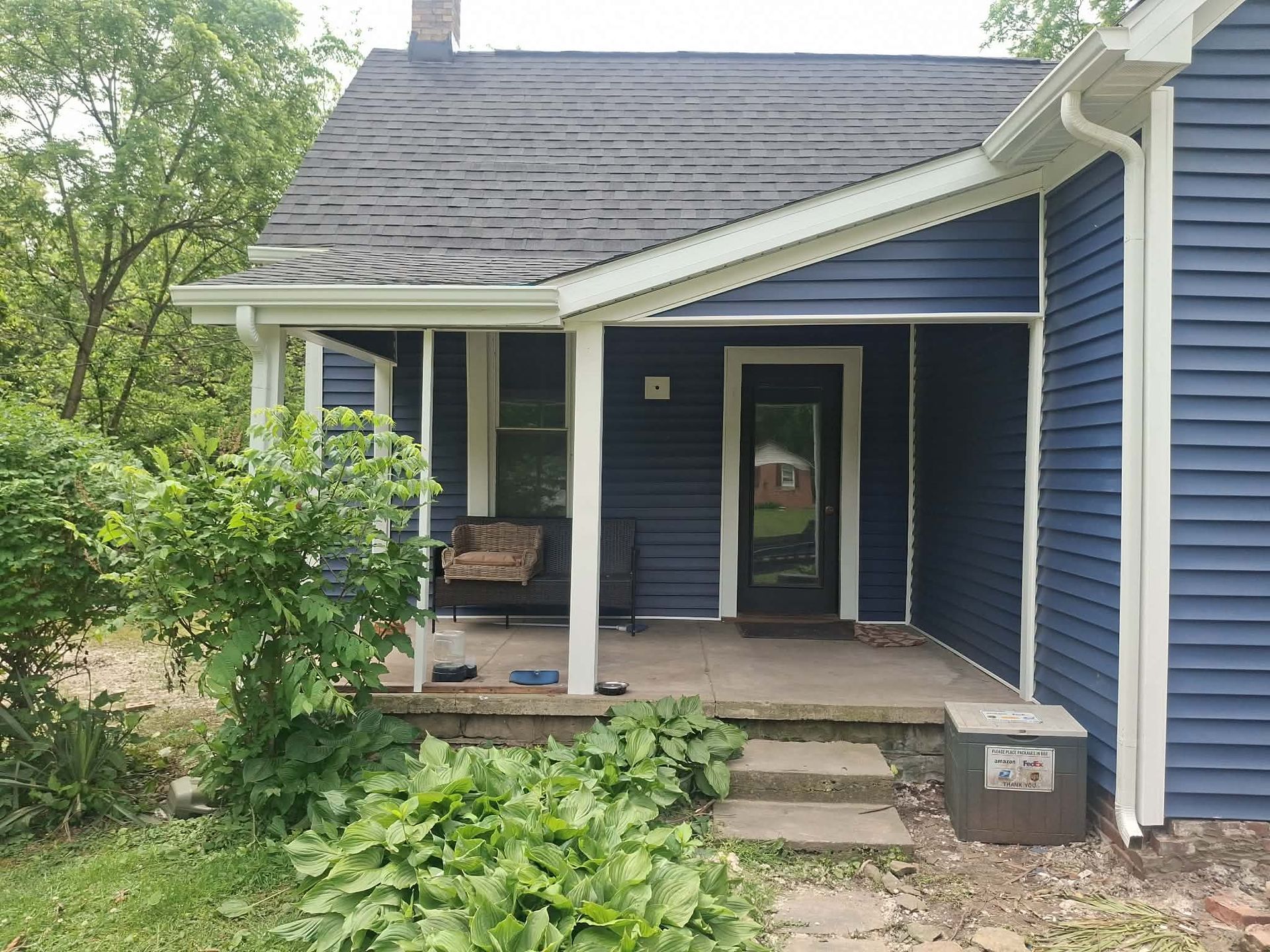 Small blue house porch with white trim, steps, and overgrown greenery in front
