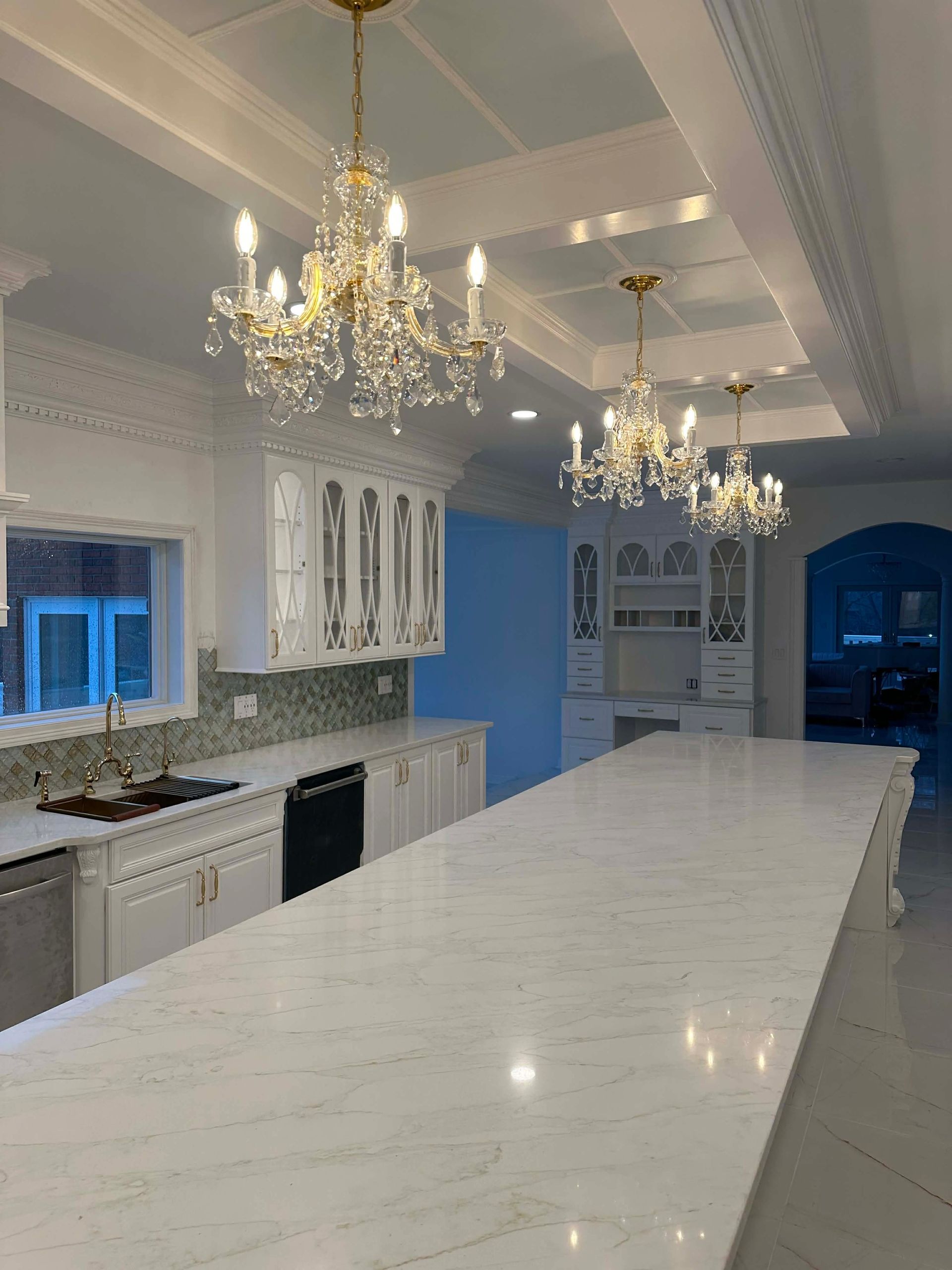Bright kitchen with white marble island, chandeliers, and blue walls
