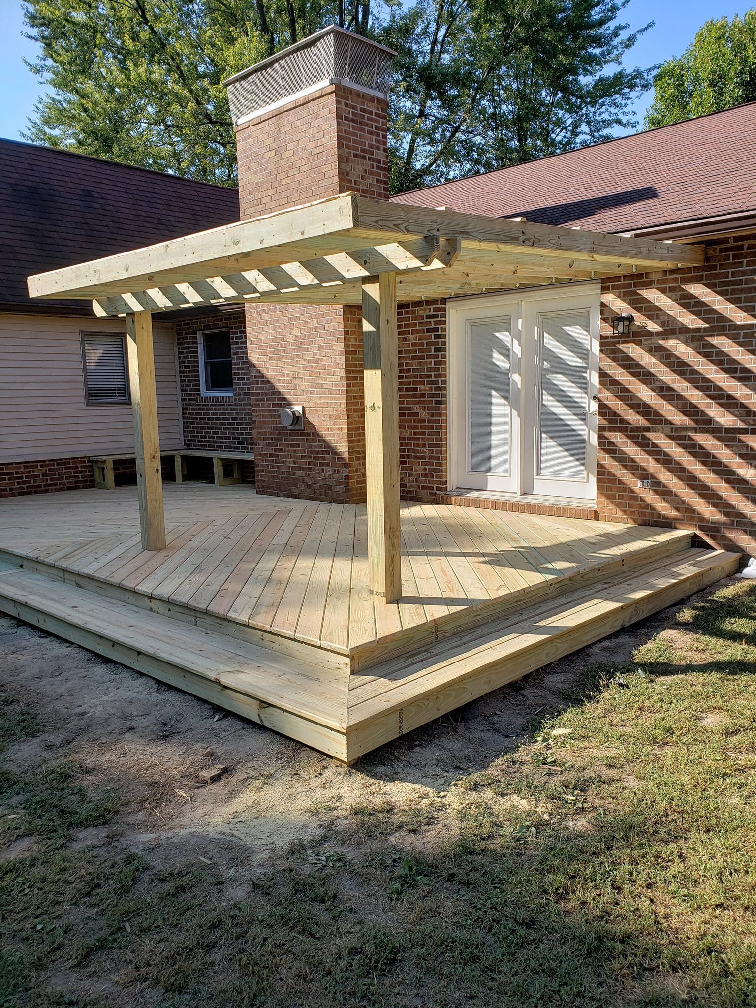 Wooden backyard deck with pergola and brick chimney attached to a house