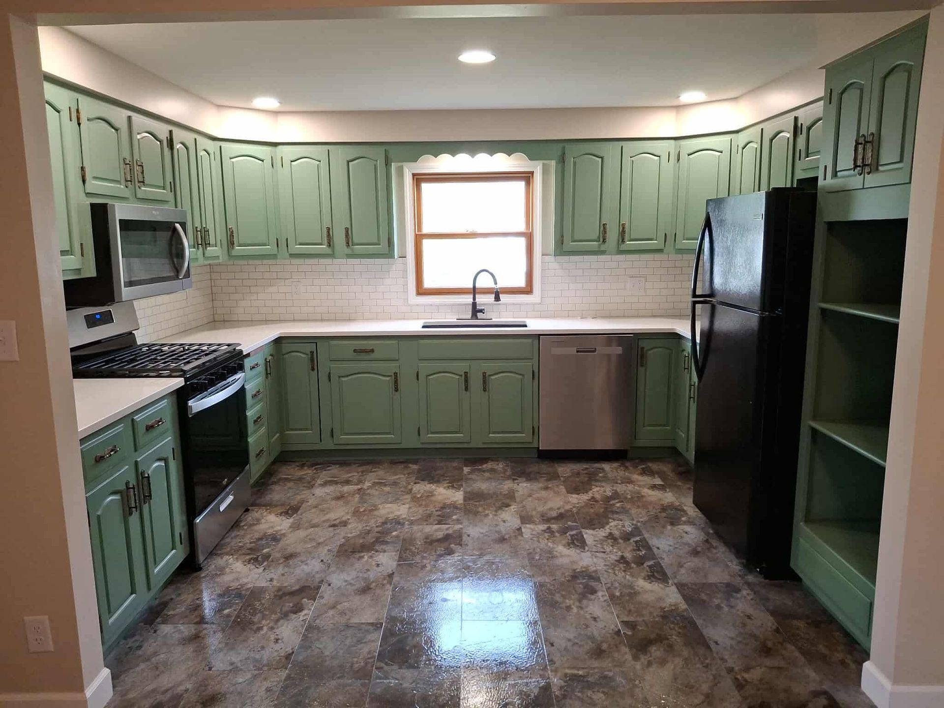 Spacious kitchen with mint green cabinets, black appliances, and a central window over the sink.