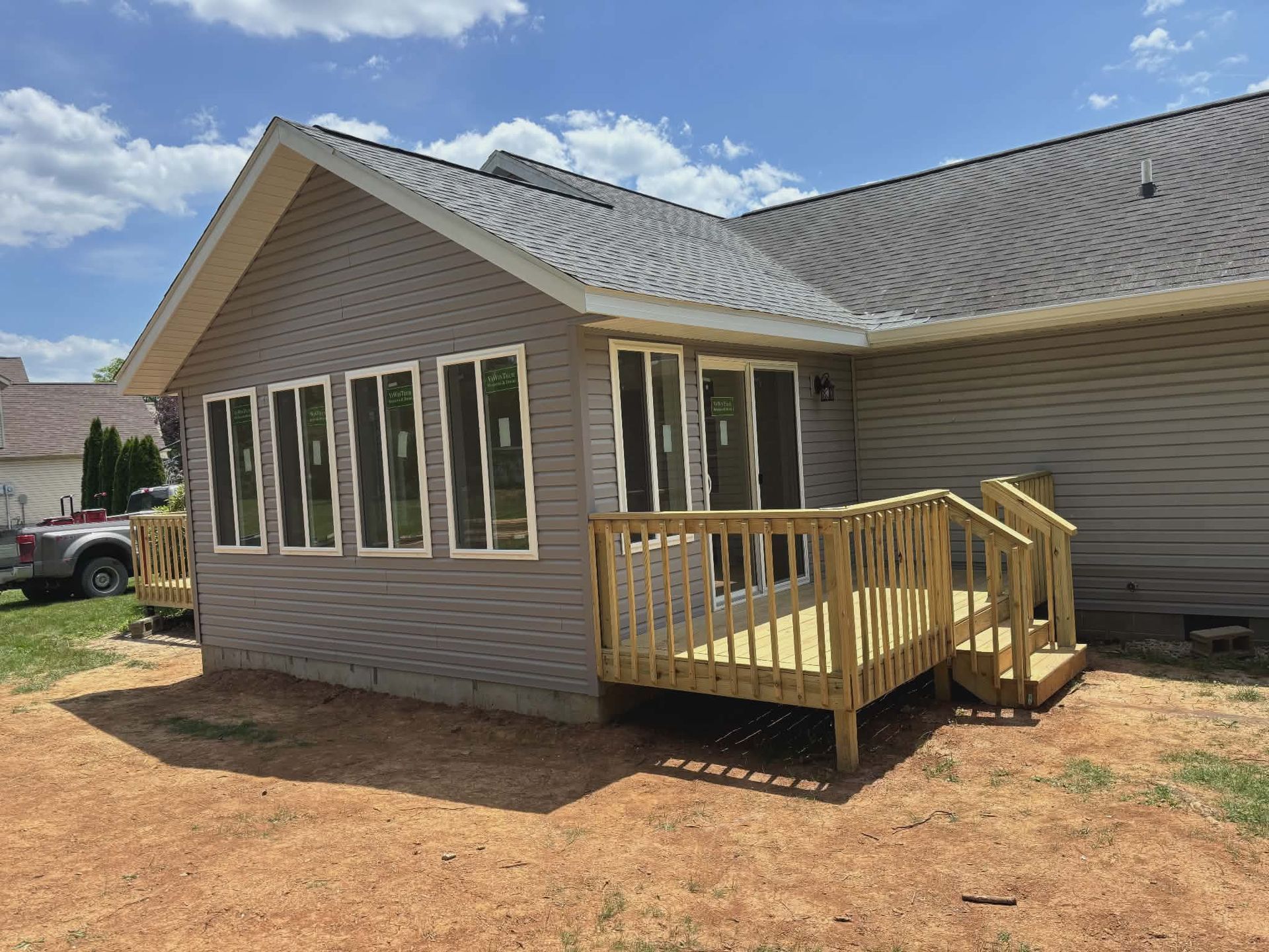 Side view of a beige house with a new wooden porch and ramp under a blue sky
