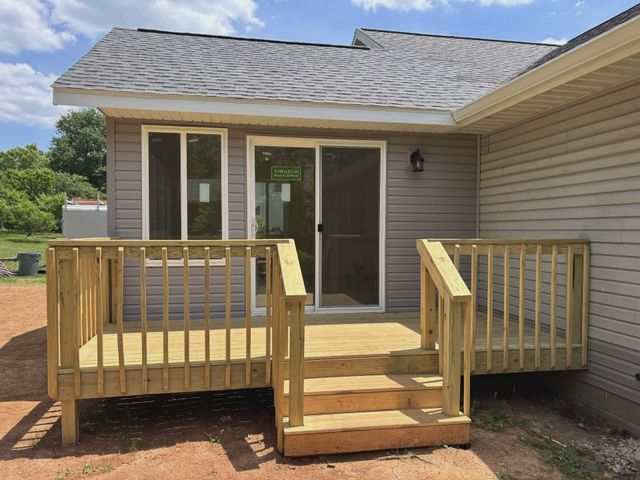 Wooden front porch with steps and railings leading to sliding glass doors on a house exterior.