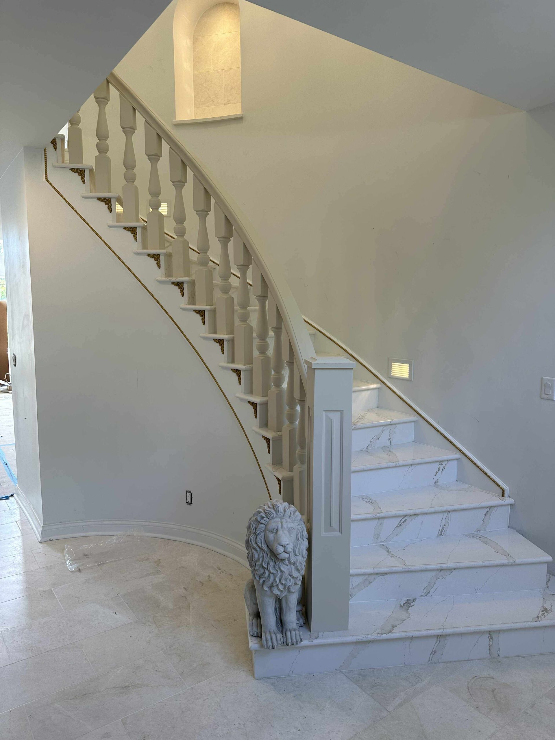 Curved staircase with white railings in a light-colored foyer, with a small statue at the base