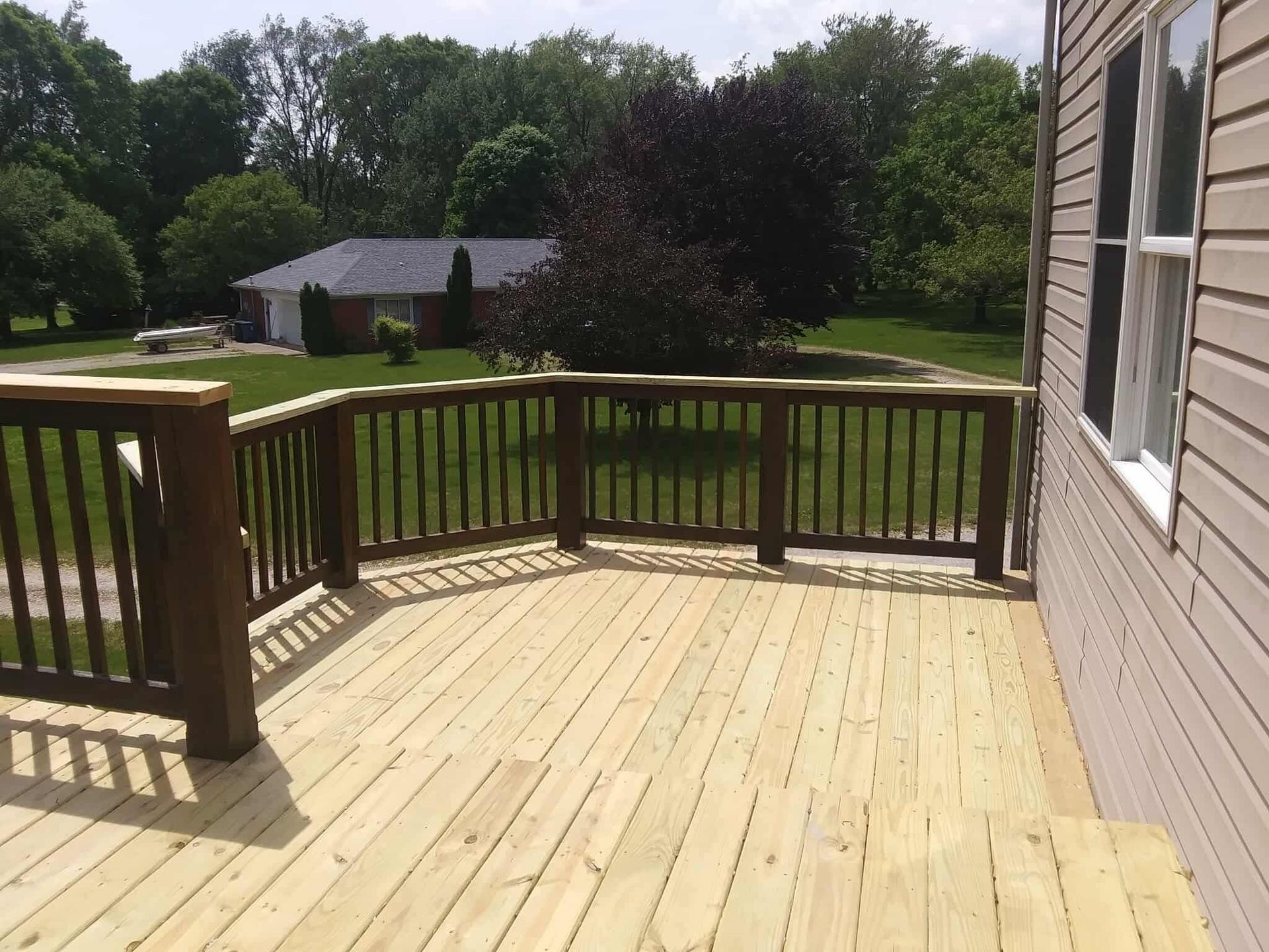 Wooden deck with railing beside a house, overlooking a grassy yard and trees