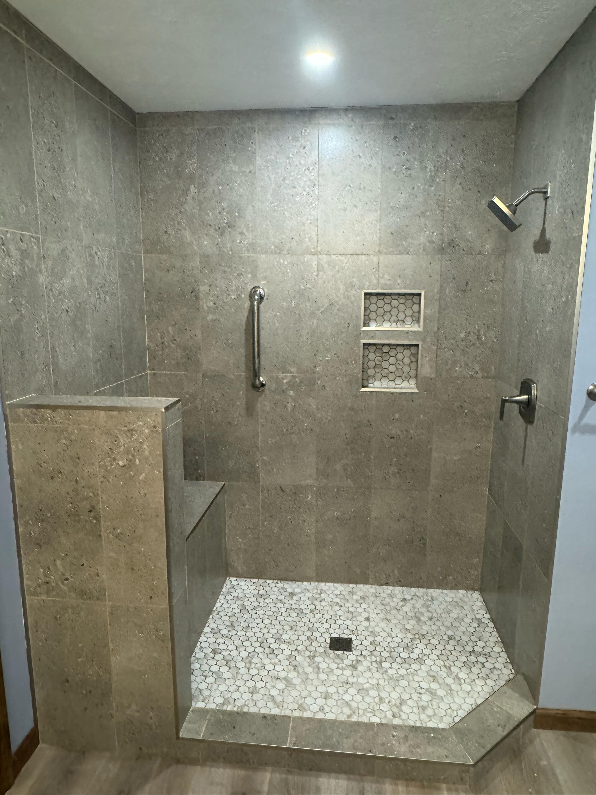 Stone-tiled walk-in shower with grab bar, built-in niche, and white pebble shower floor.