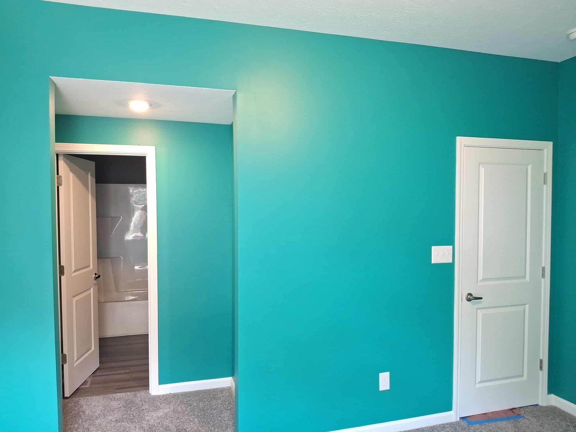 Turquoise bedroom with white doors and a view into a bathroom through the doorway