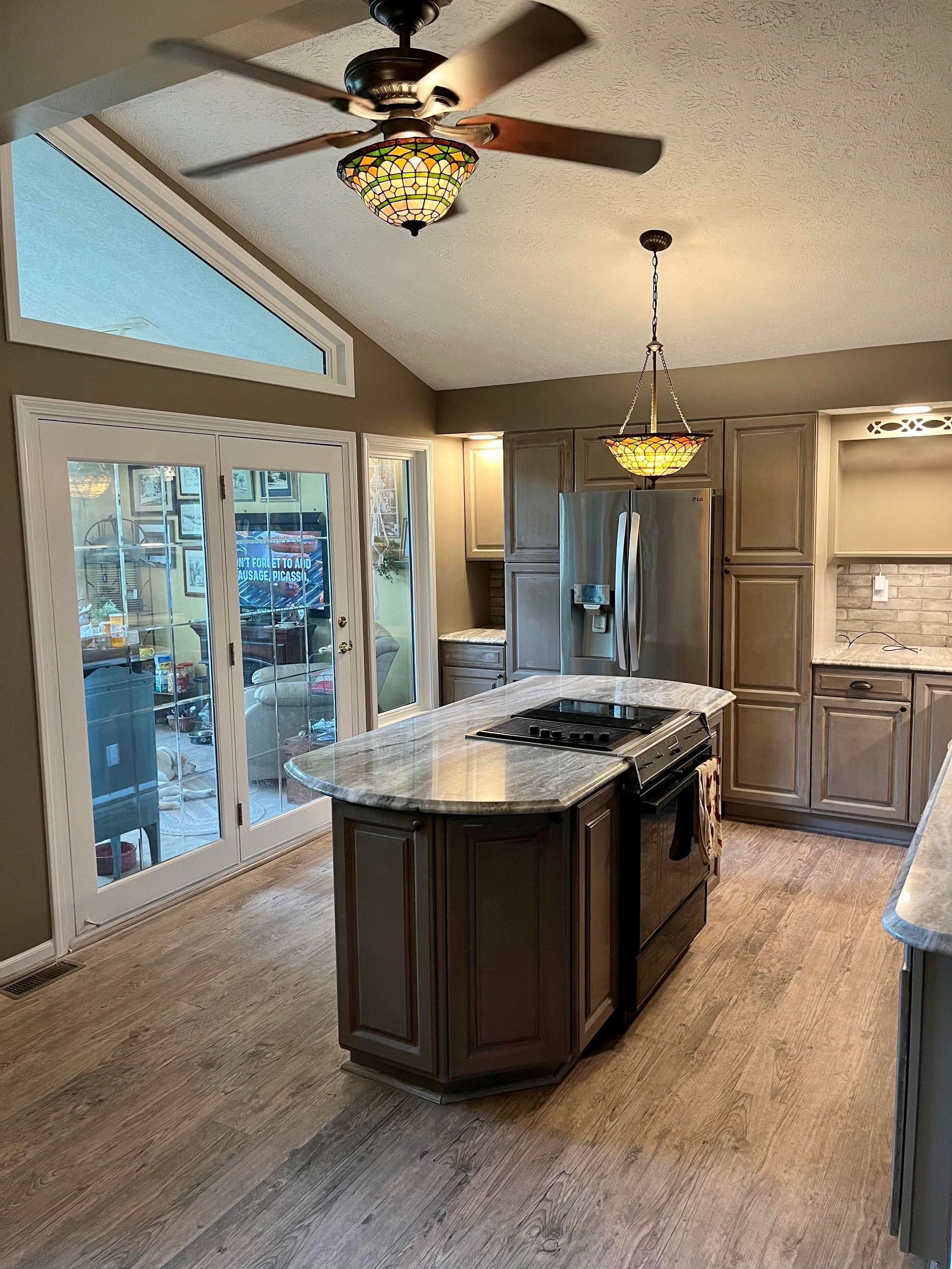 Modern kitchen with island, granite countertops, pendant lights, and large windows by a dining nook