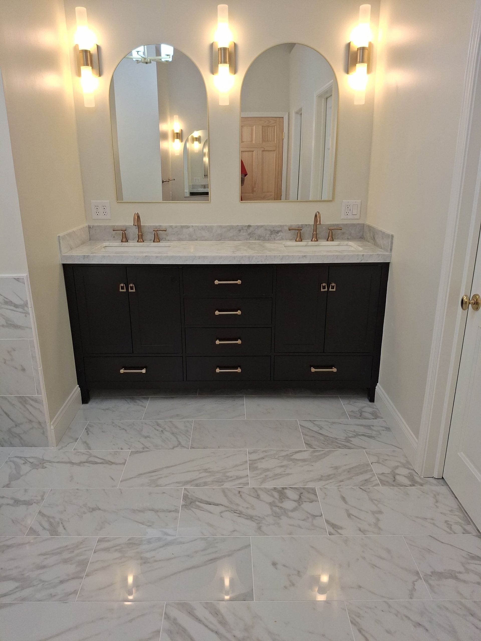 Modern bathroom with black vanity, double mirrors, wall sconces, and white marble tile floor.
