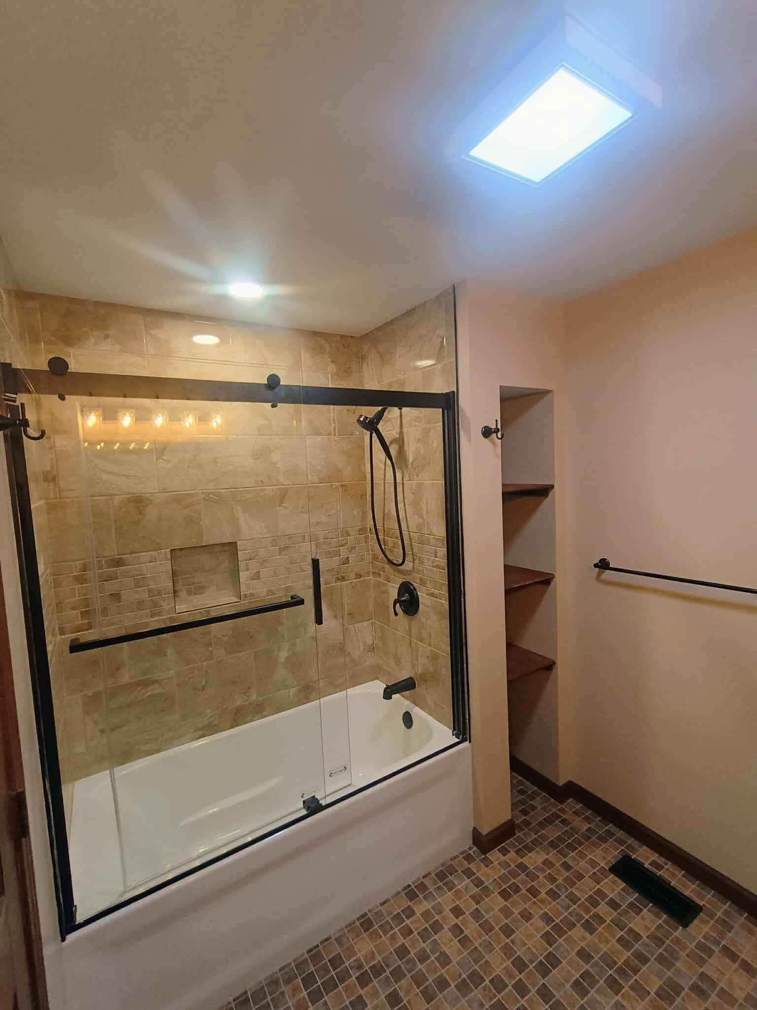 Small bathroom with a tiled shower-tub, glass enclosure, beige walls, and patterned floor.