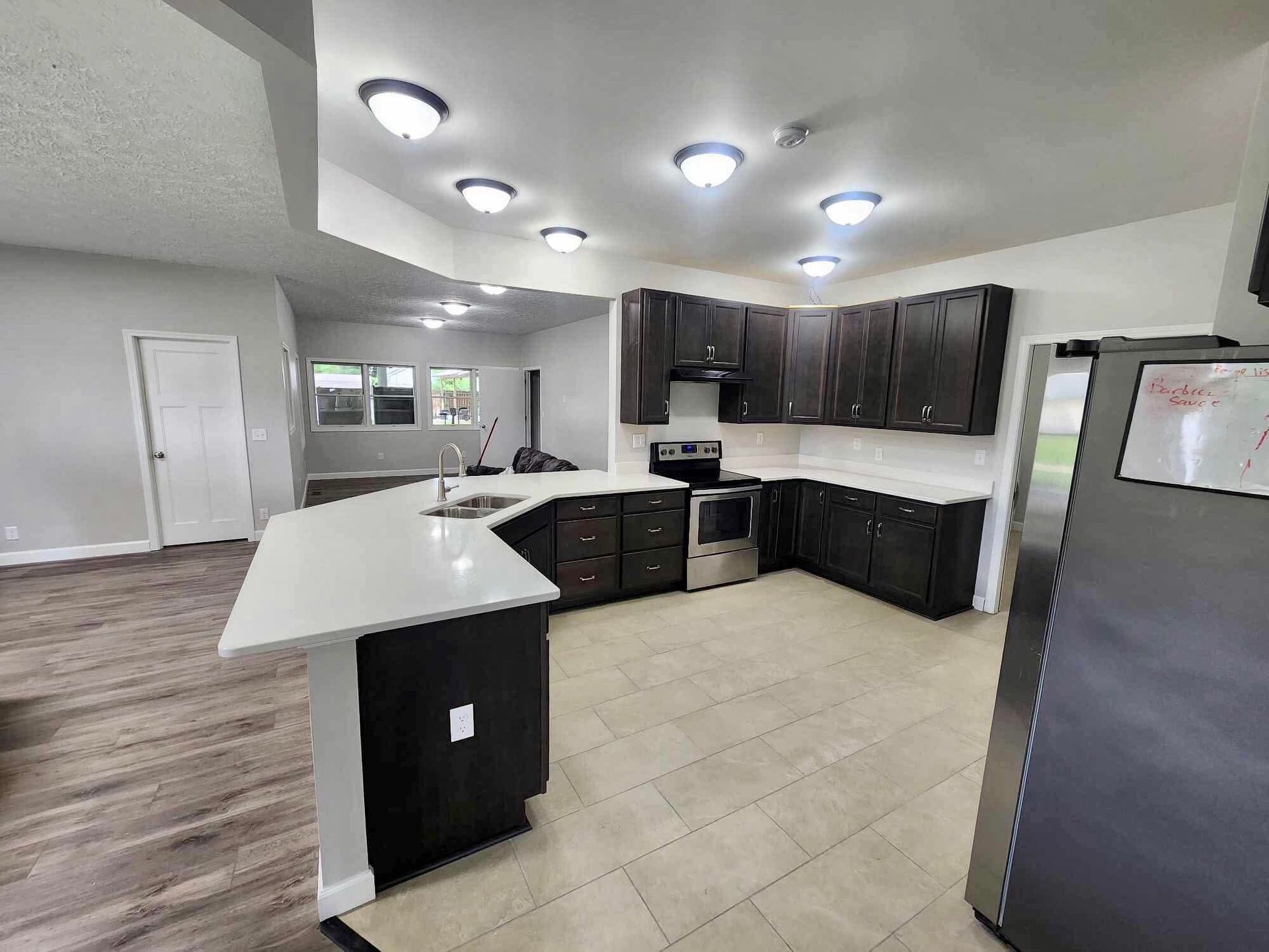 Modern kitchen with dark cabinets, white island, tiled floor, and bright ceiling lights.