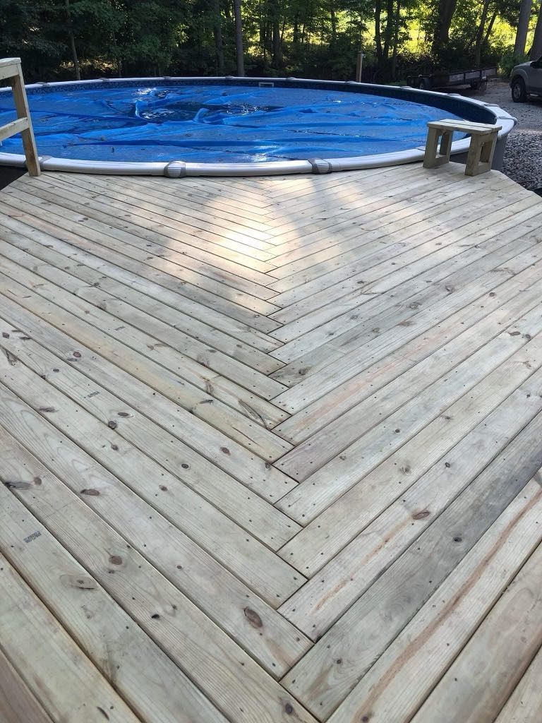 Wooden deck with a blue-covered above-ground pool in a wooded backyard