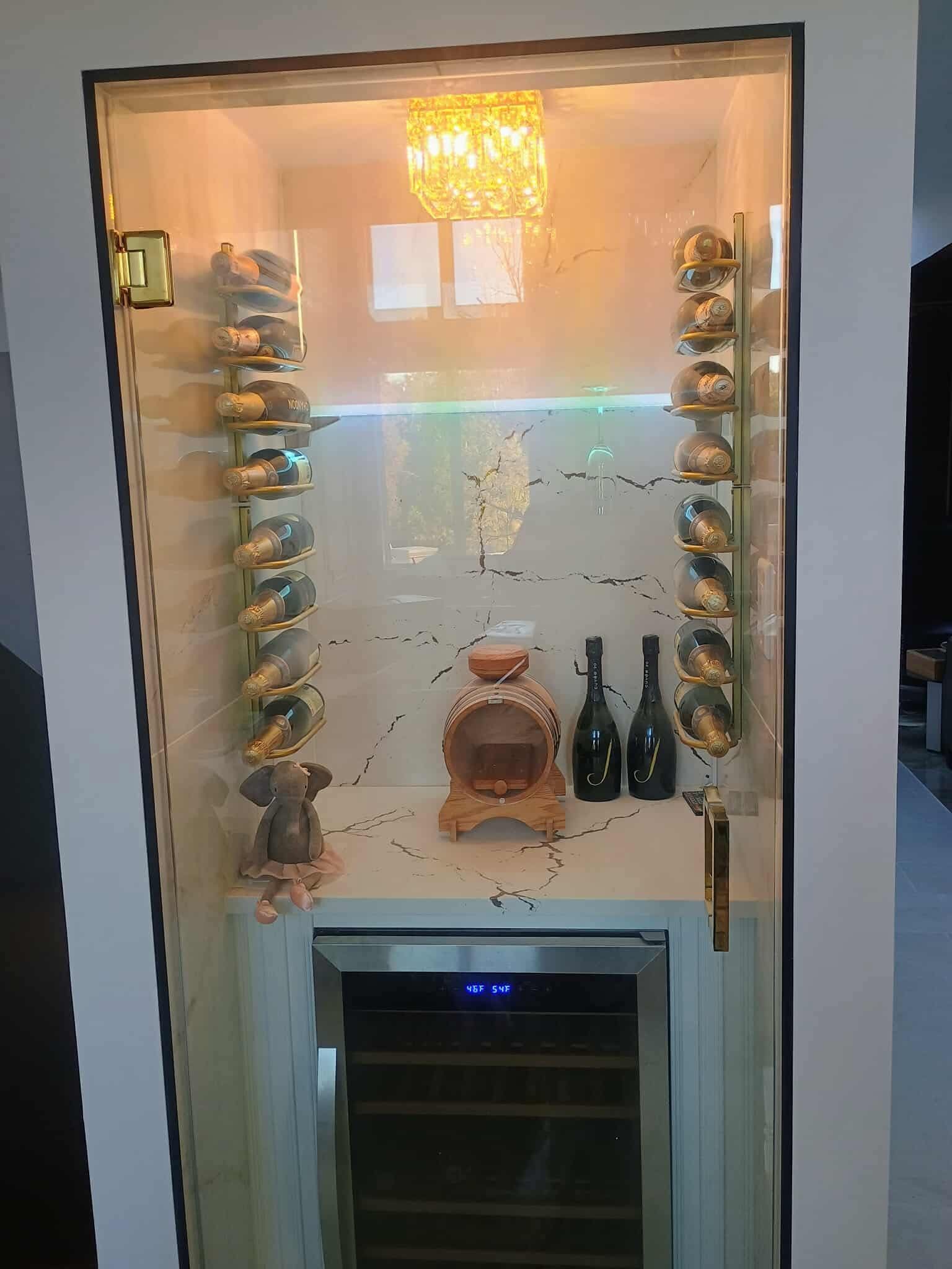 Decorative hallway niche with lit shelves, a small statue, hanging chandelier, and a mini fridge below
