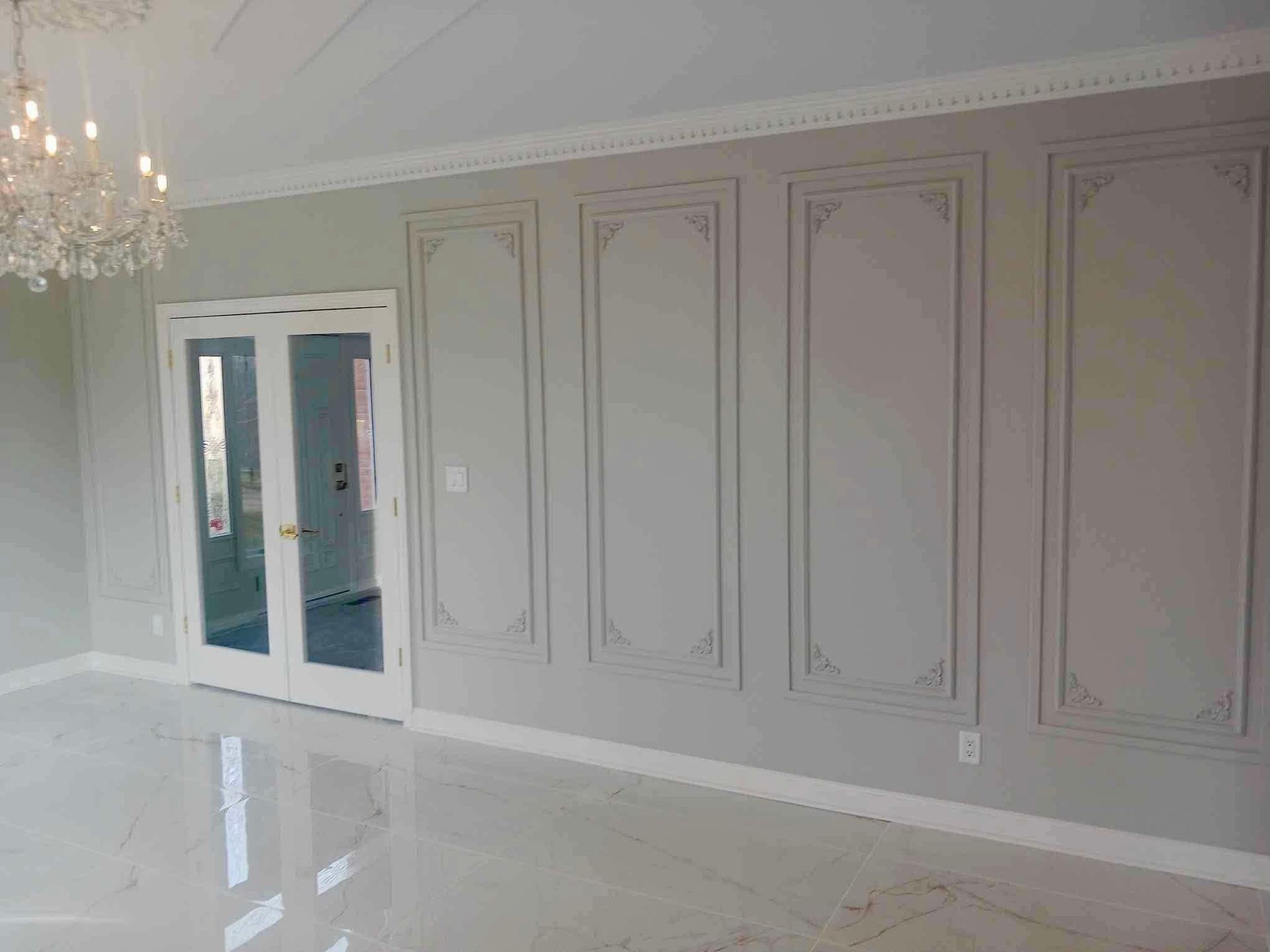 Elegant gray living room with paneled wall, glass double doors, chandelier, and glossy floor