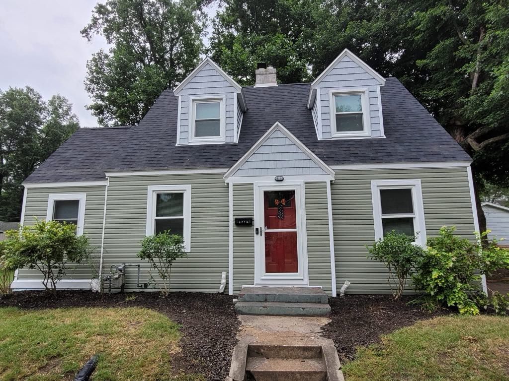 Gray house with red front door, white trim, and dormer windows, fronted by a small walkway and shrubs