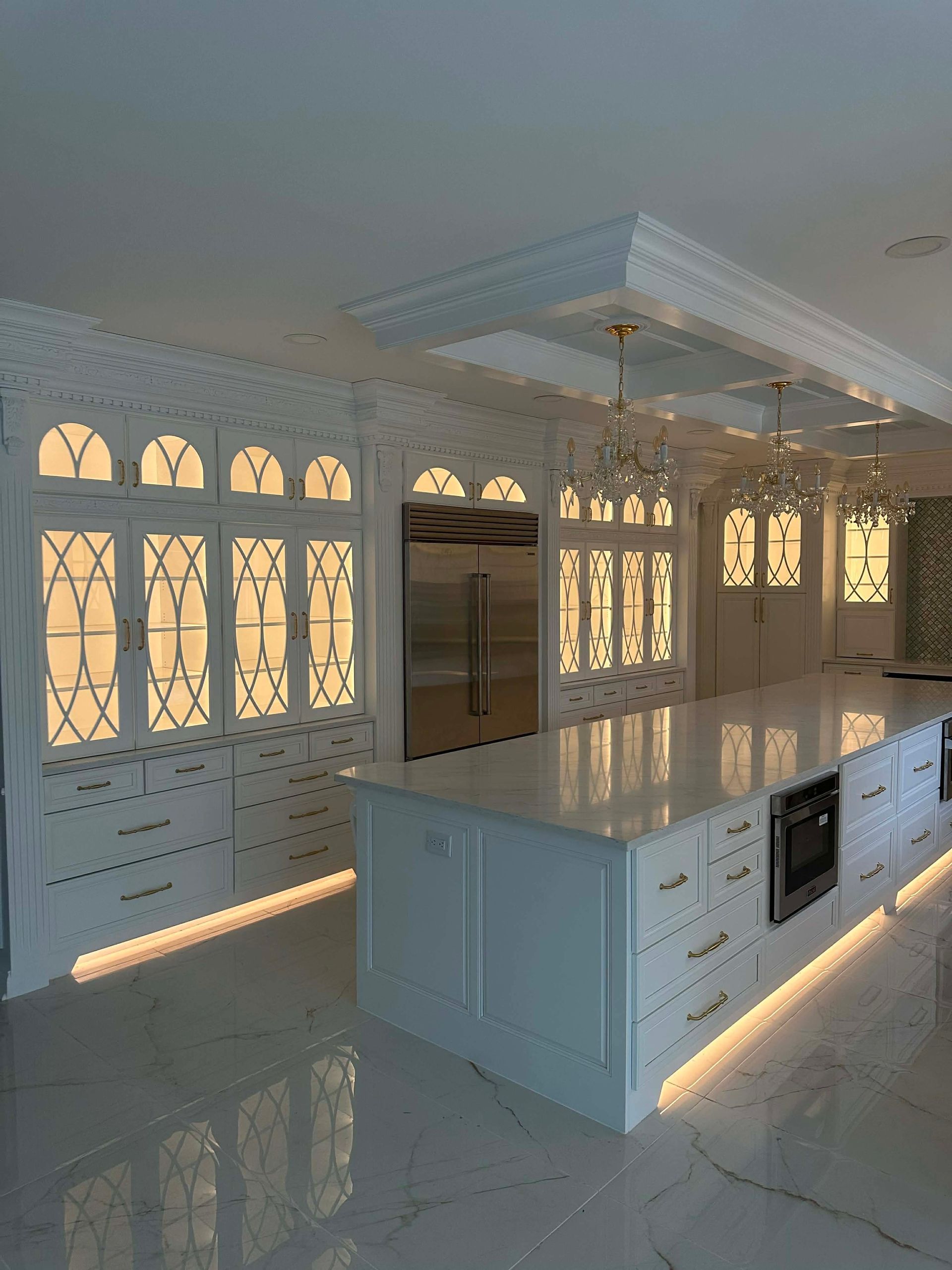 Bright modern kitchen with white cabinets, marble island, and sunlight casting window shadows on the floor.
