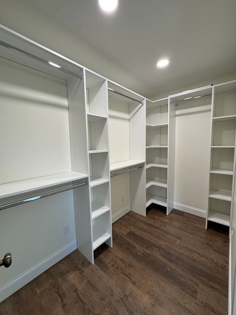 White walk-in closet with built-in shelves, hanging rods, and dark wood floor