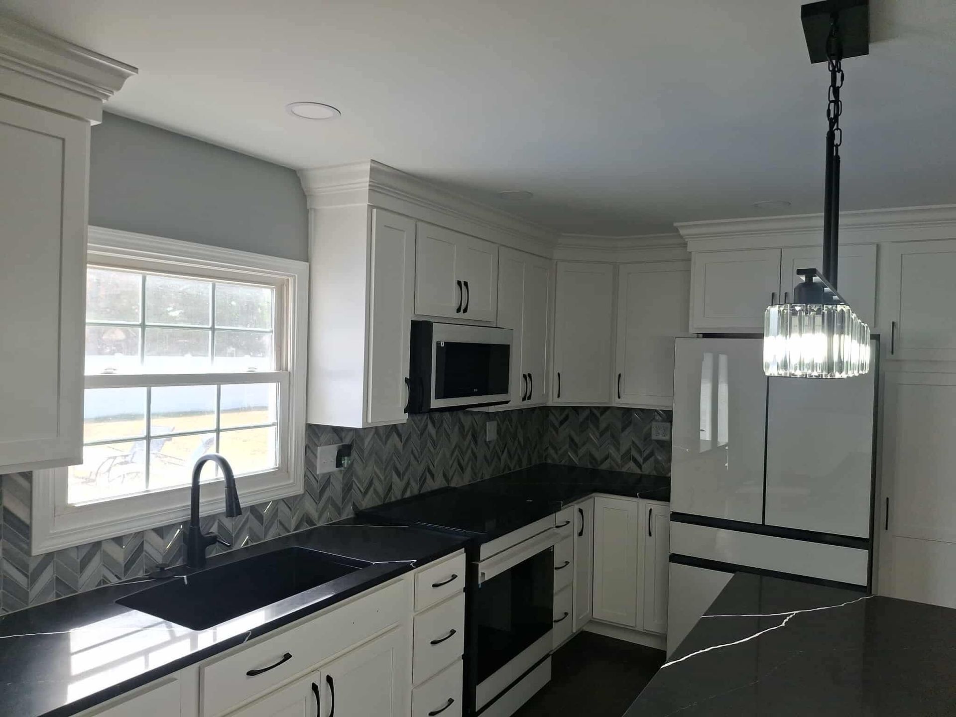 Bright white kitchen with black countertops, window, island sink, and hanging pendant light