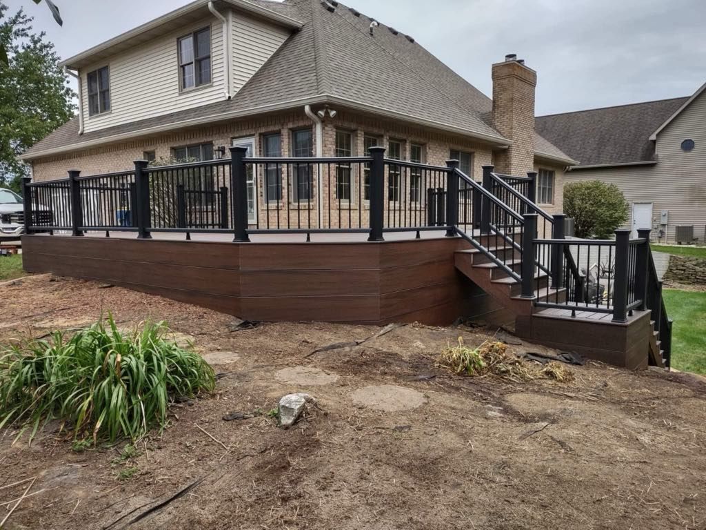 House with raised deck, black railings, and stairs in a landscaped yard