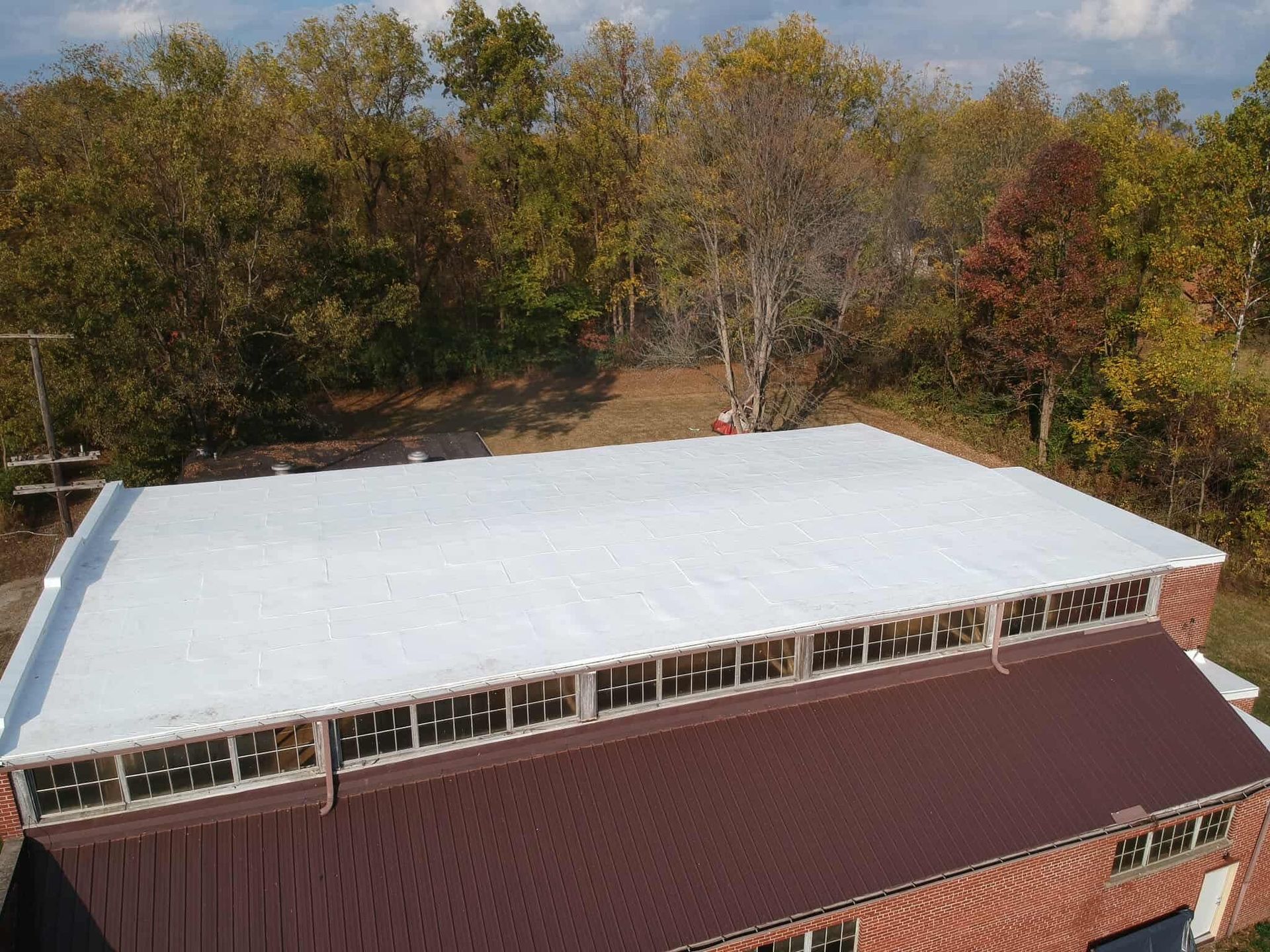 Rooftop covered with white material beside a red building, seen from above with trees in the background