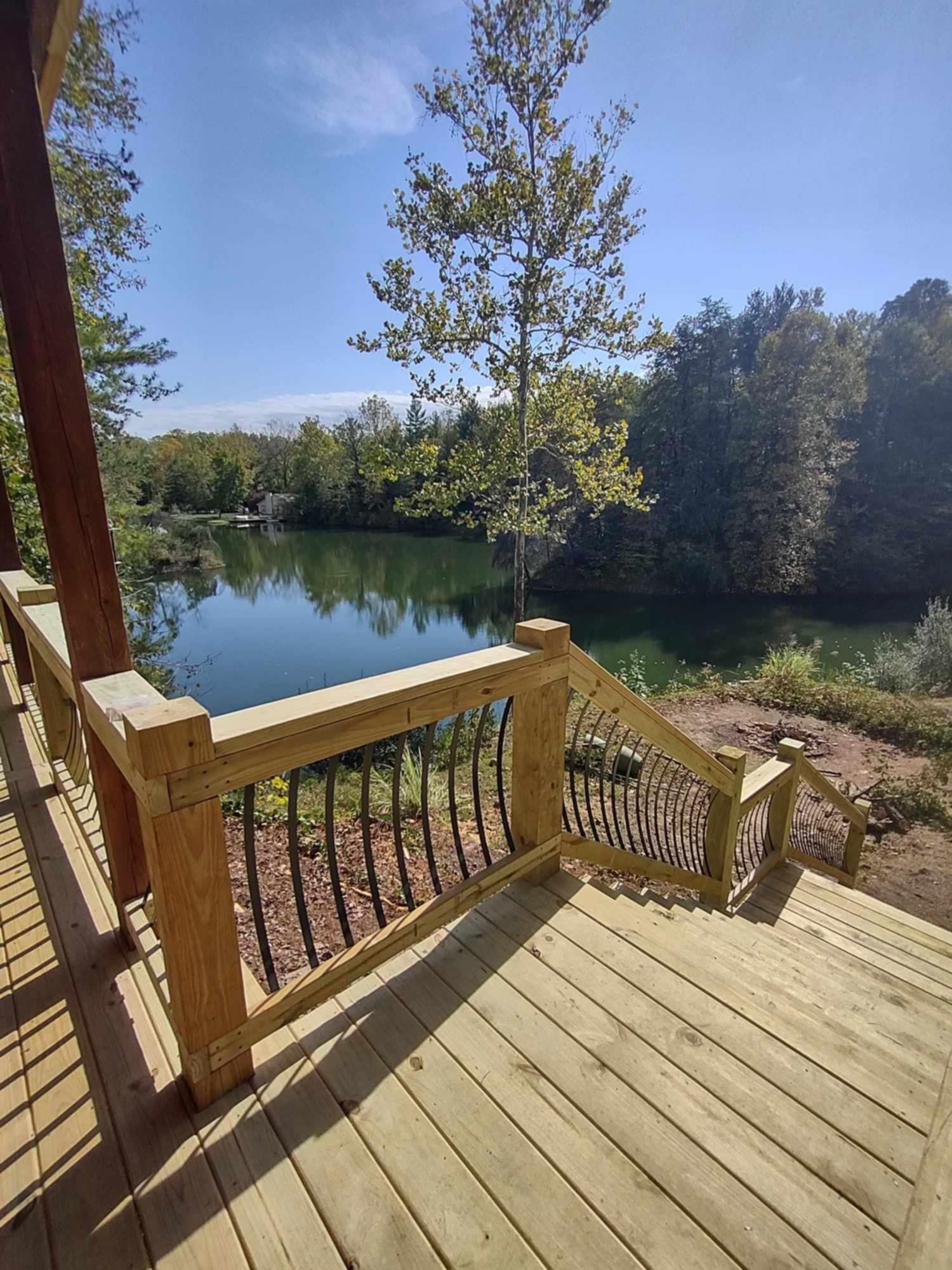 Wooden deck stairs overlooking a calm lake surrounded by trees on a sunny day
