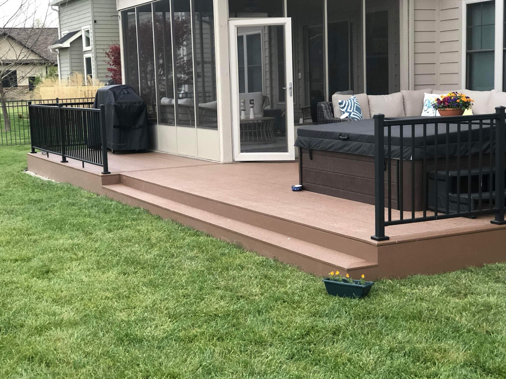 Backyard deck with black railing, tan flooring, grill, and patio furniture beside a grassy lawn