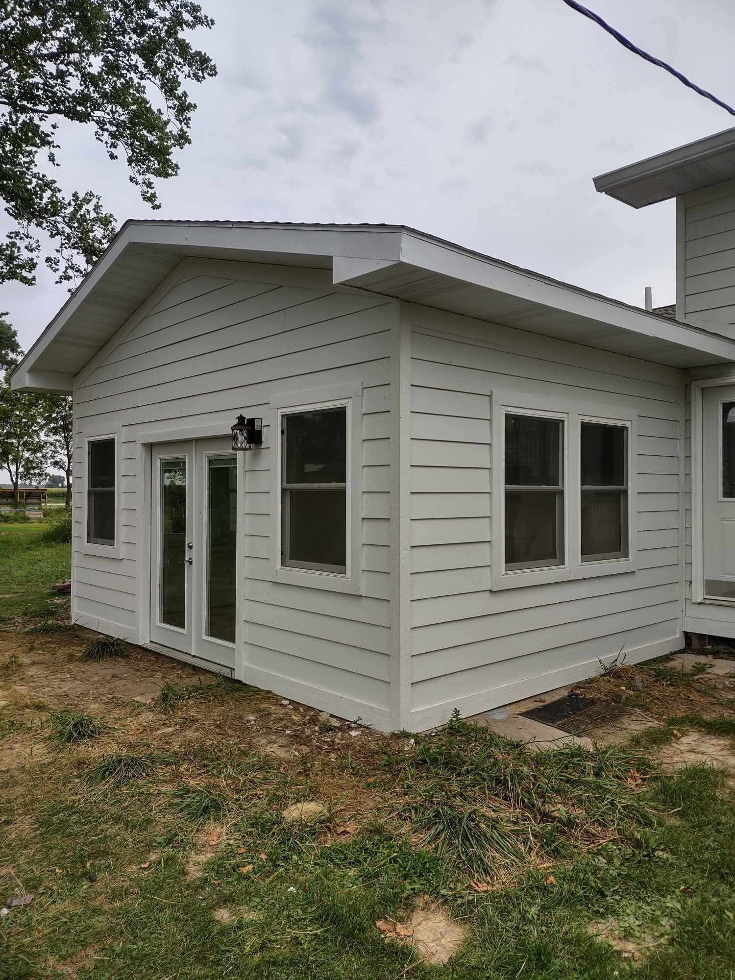 Small white house addition with horizontal siding, multiple windows, and a sloped roof in a grassy yard