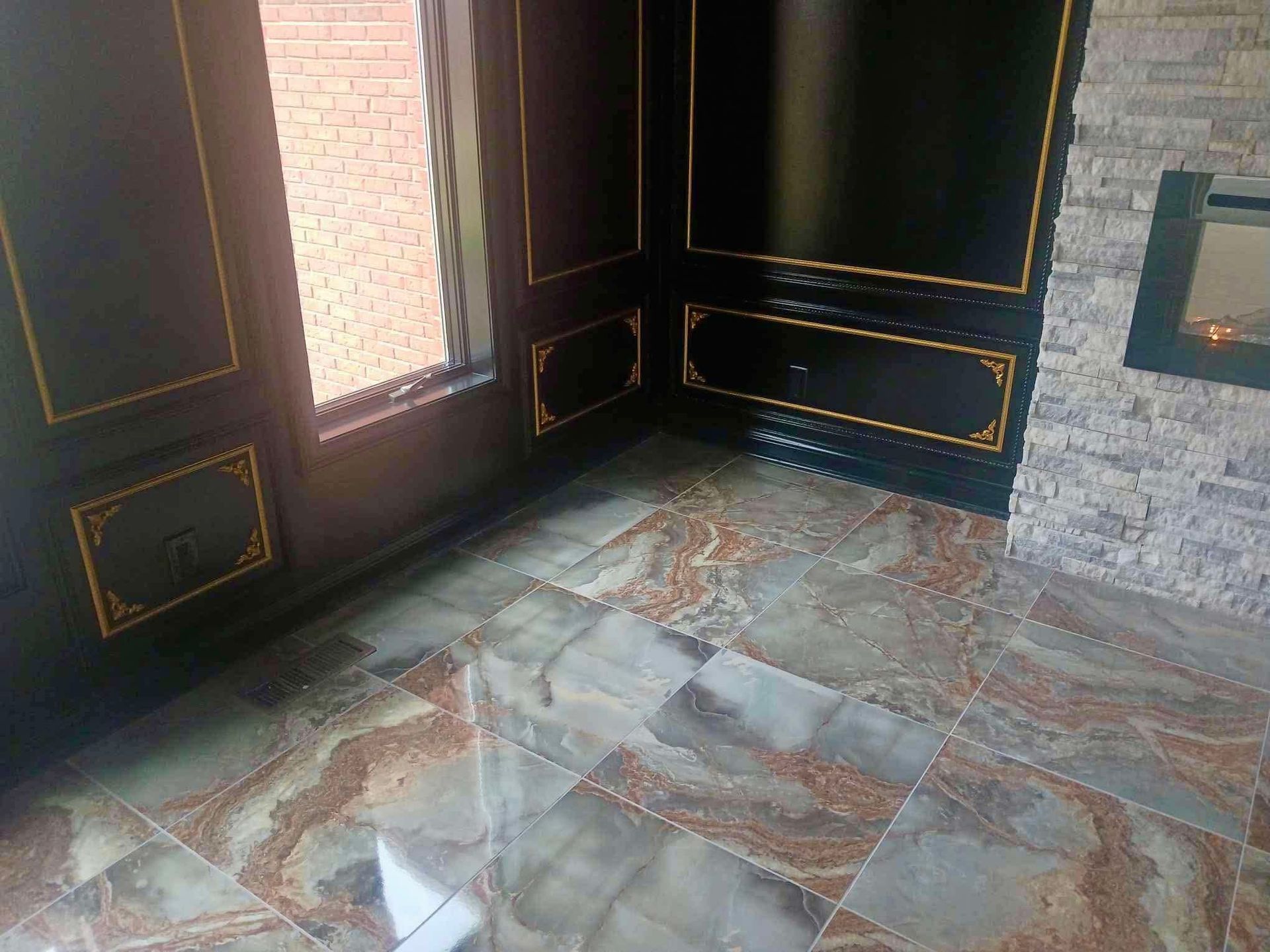 Empty room with dark paneled walls, gold trim, and a glossy gray-brown tiled floor.