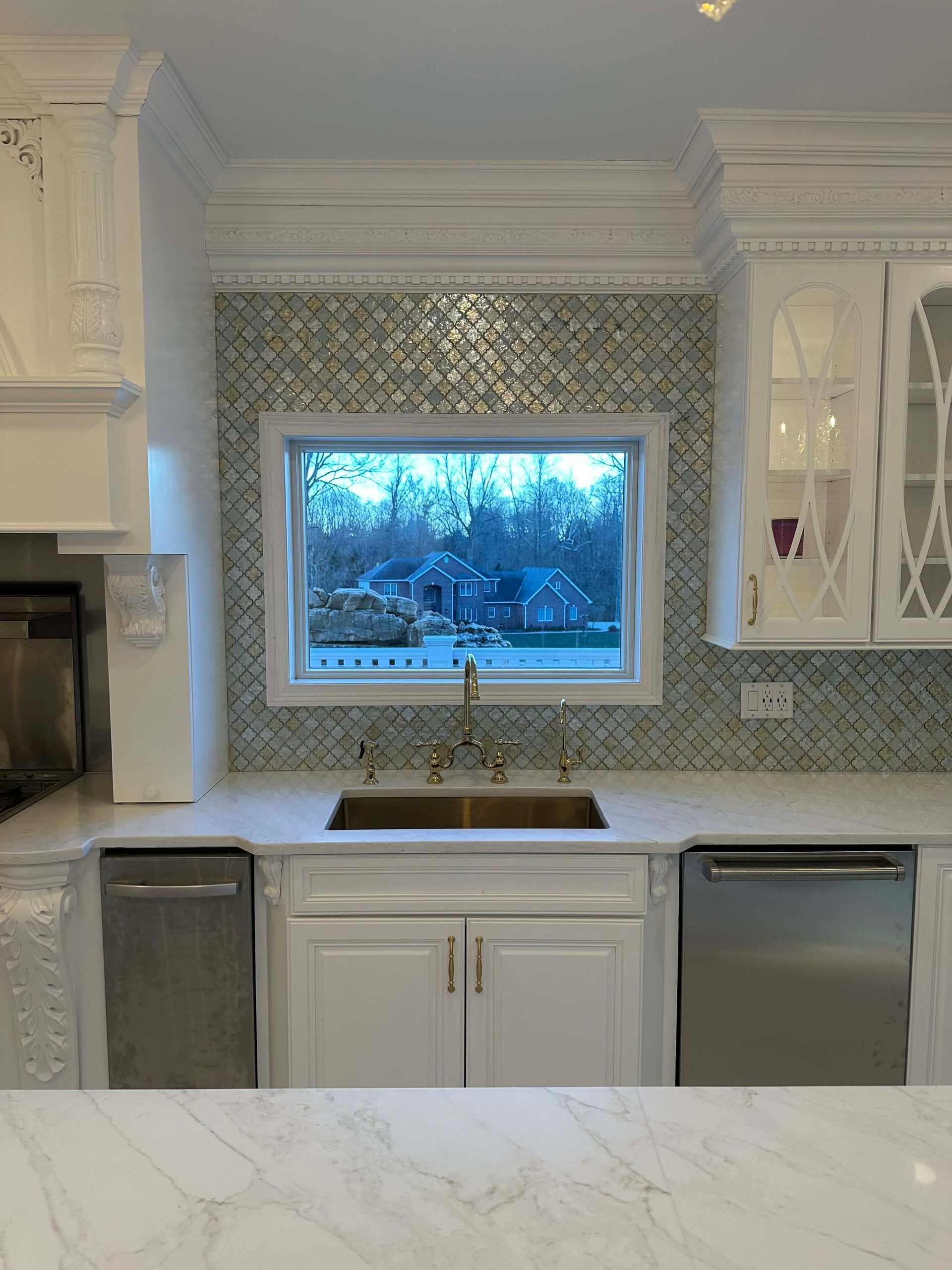 White kitchen with patterned backsplash, window over sink, and stainless steel dishwasher and trash bins.