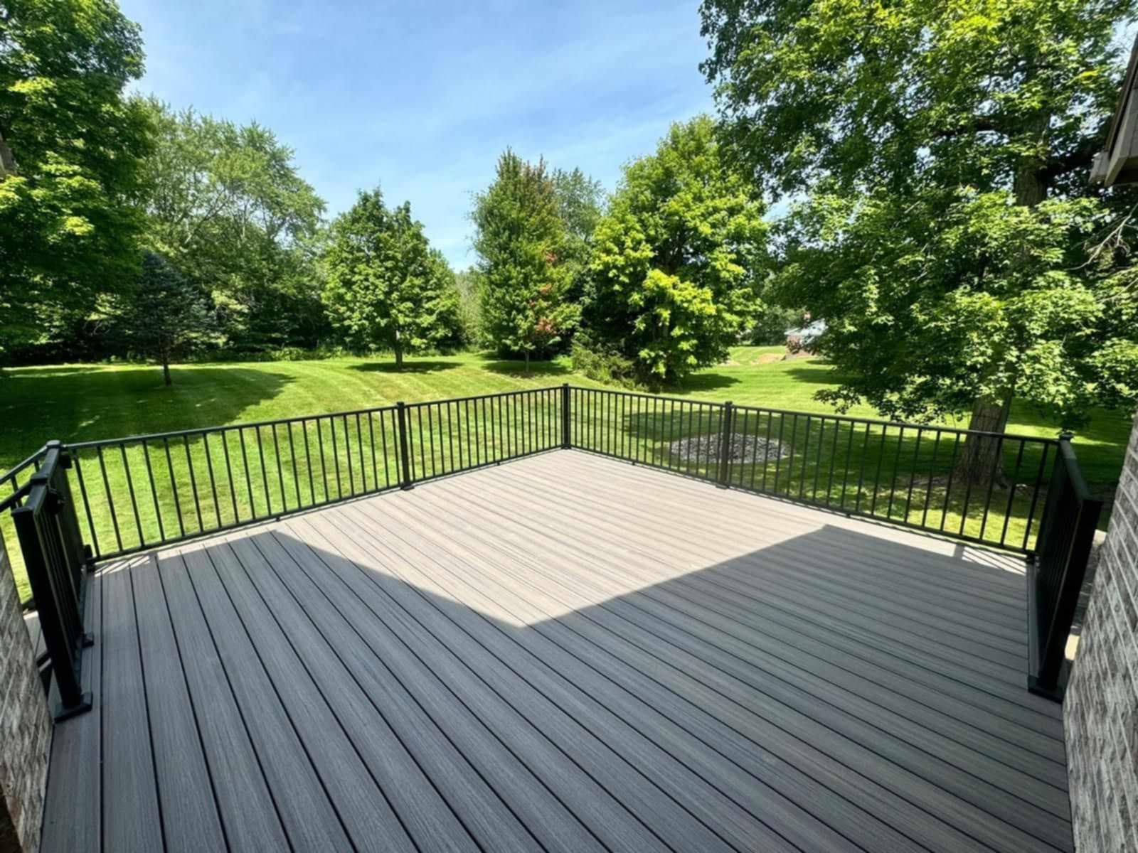 Wooden deck overlooking a green park with trees and black railings.