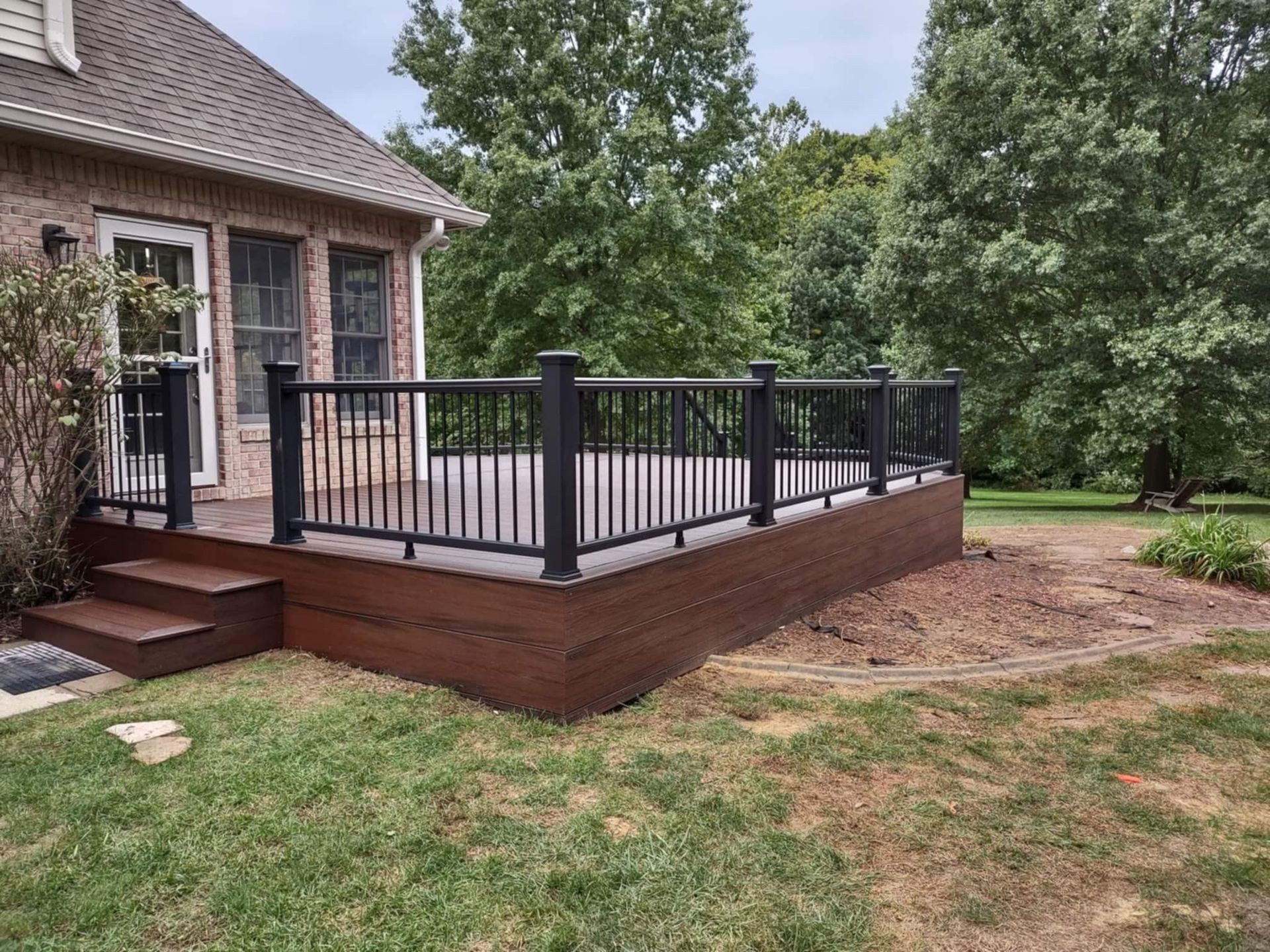 Backyard deck with black railing beside a brick house and grassy yard