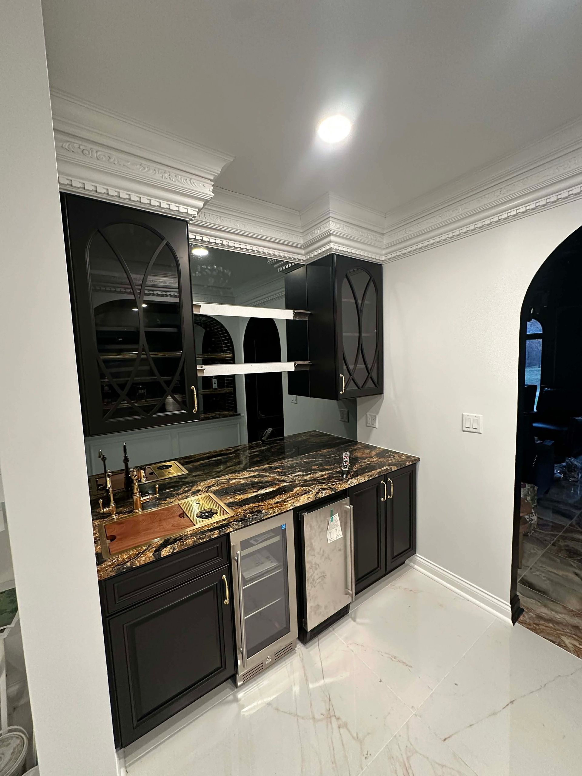 Elegant modern kitchen with black cabinets, marble counters, and white tile floor